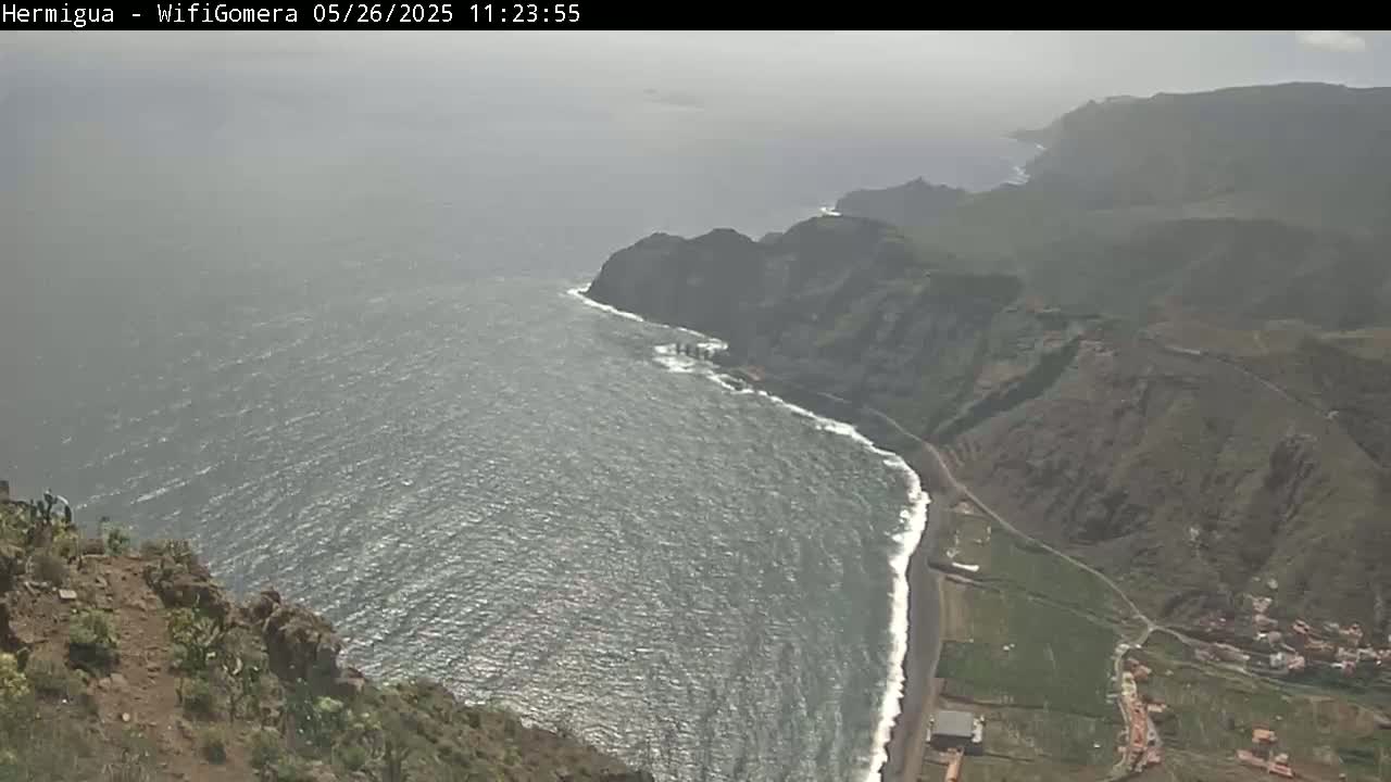 A hazy view shows a dark, rocky coastline meeting a choppy ocean under a gray sky.