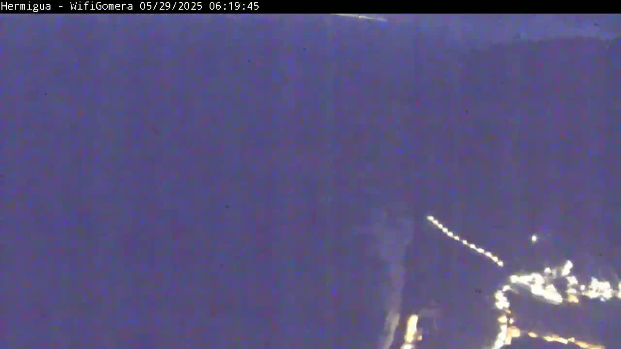 A blurry, nighttime image shows a small cluster of lights in the lower right corner against a dark purple background.