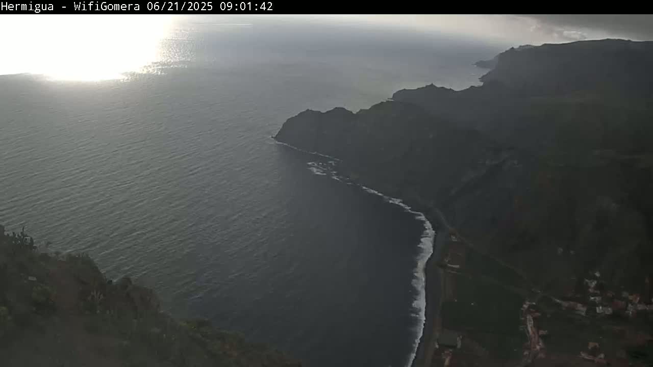 A high-angle view shows a dark-colored ocean meeting a rugged coastline under overcast skies.