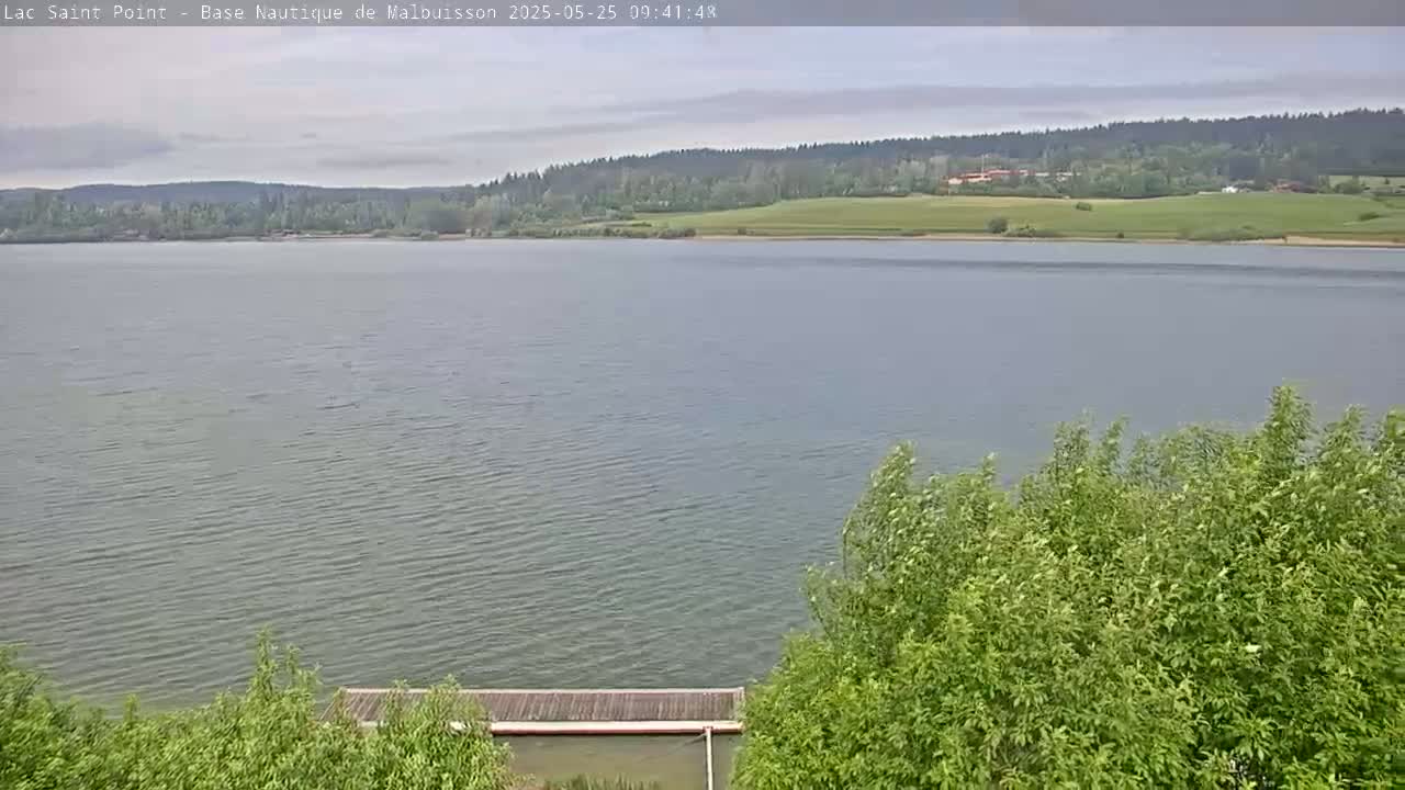 A calm lake stretches out to a distant, tree-covered shoreline under an overcast sky.