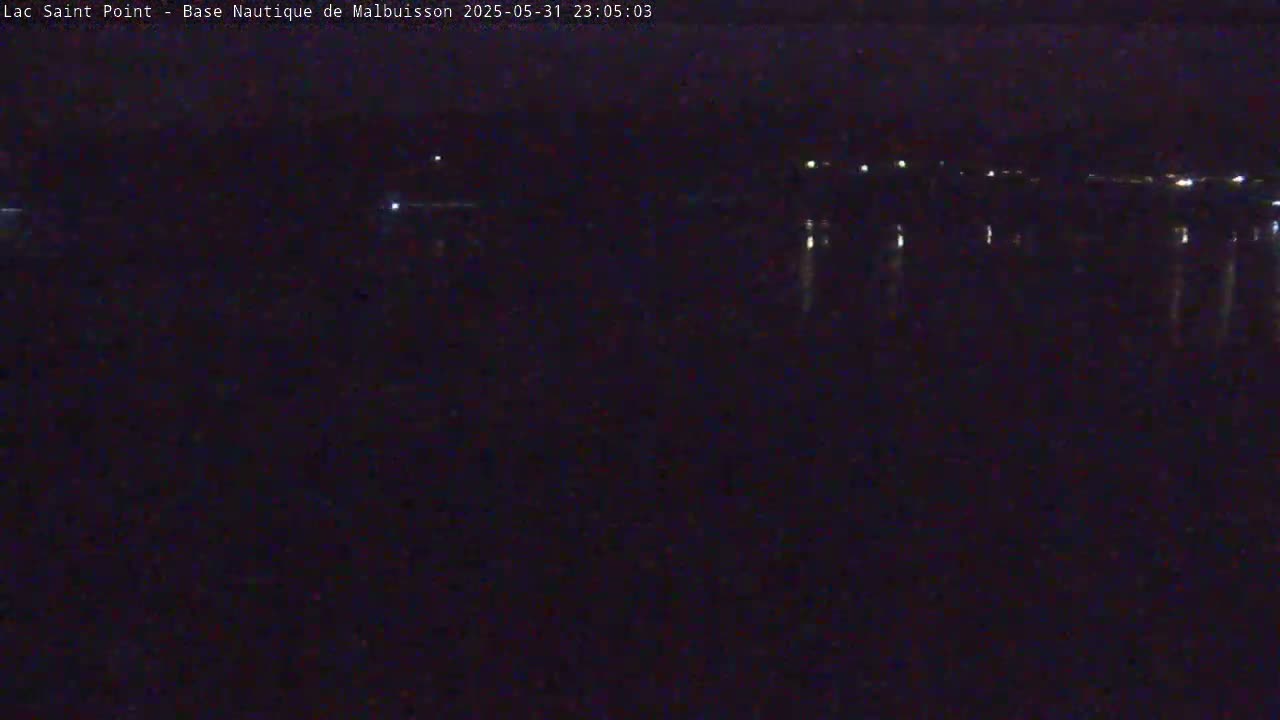 A dark, nighttime view of a body of water reflecting a few distant lights.