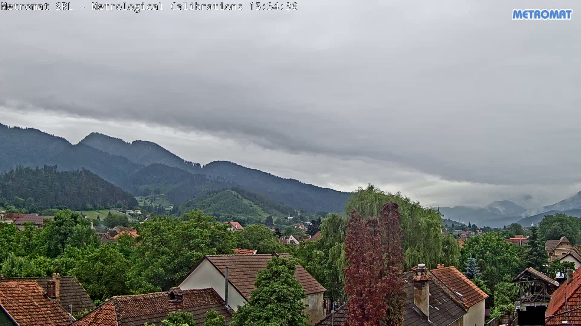 A view of a town nestled among green, tree-covered hills and mountains under an overcast sky.