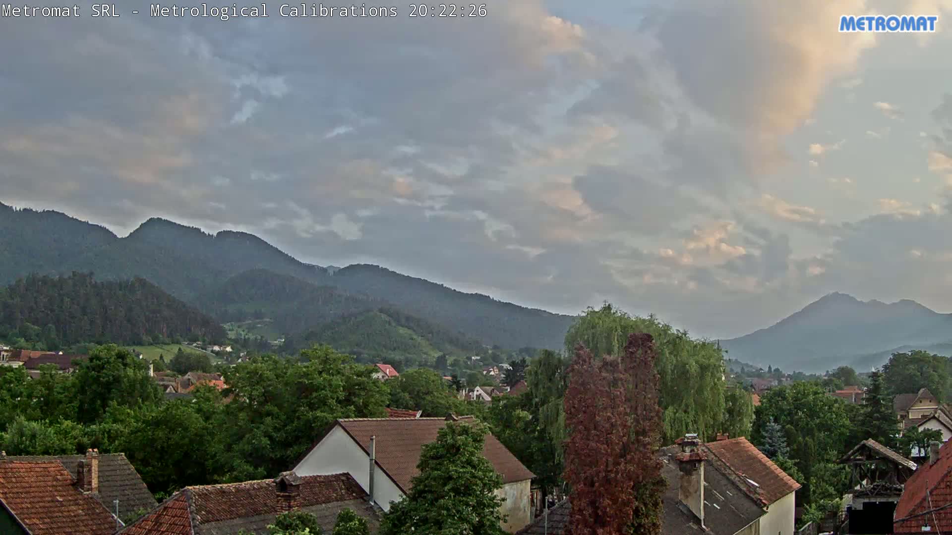 A partly cloudy sky hangs over a small town nestled at the foot of a mountain range.