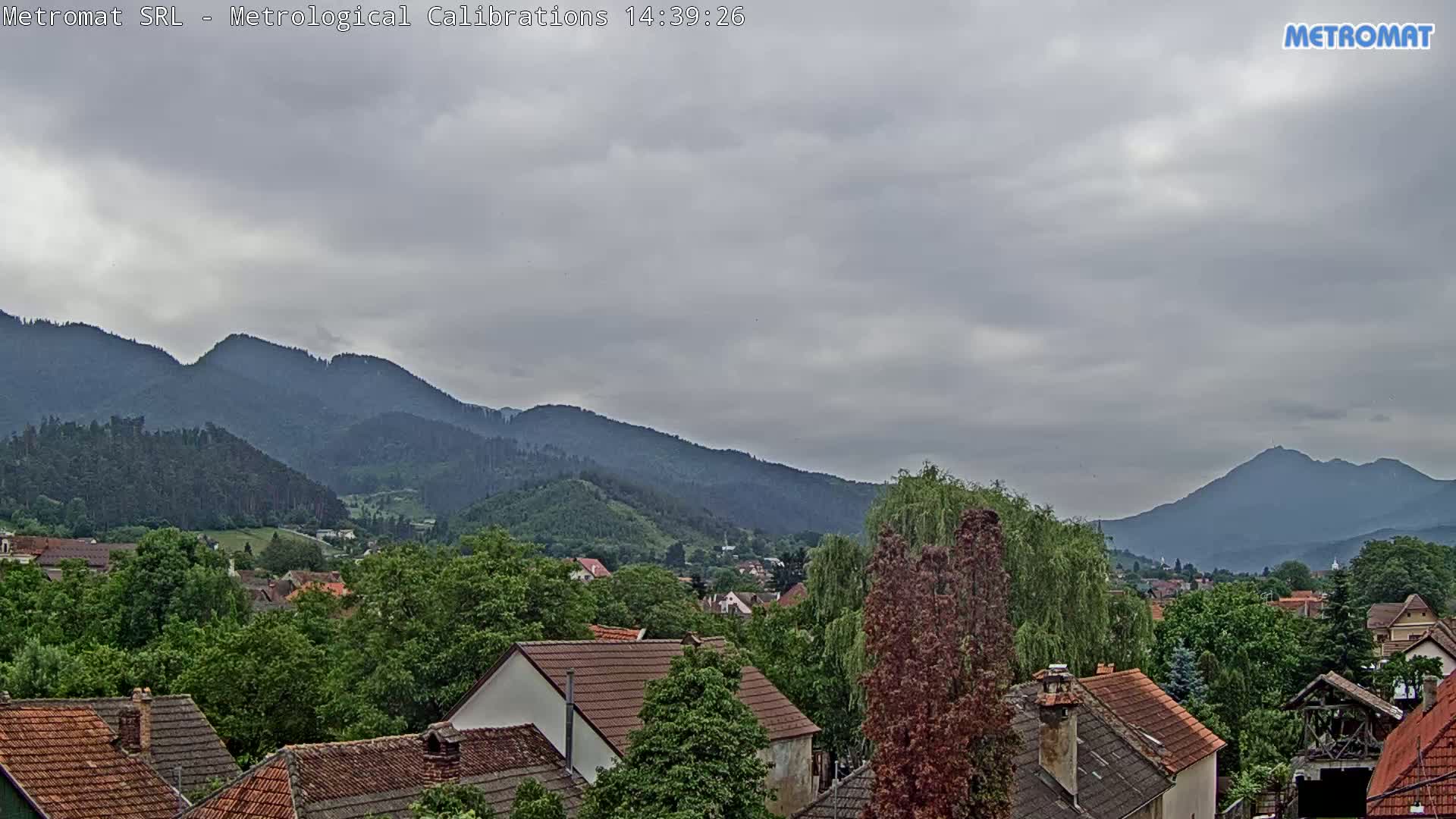 A view of a town nestled among green hills and mountains under an overcast sky.