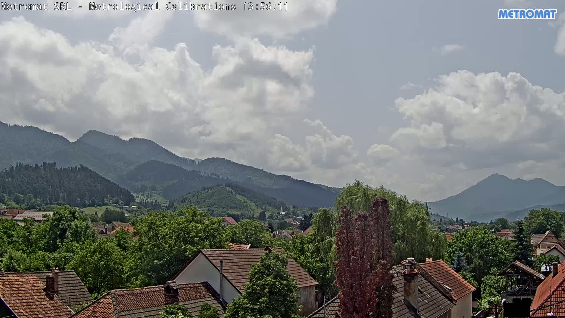 A partly cloudy sky overlooks a town nestled amongst green, tree-covered hills and mountains.