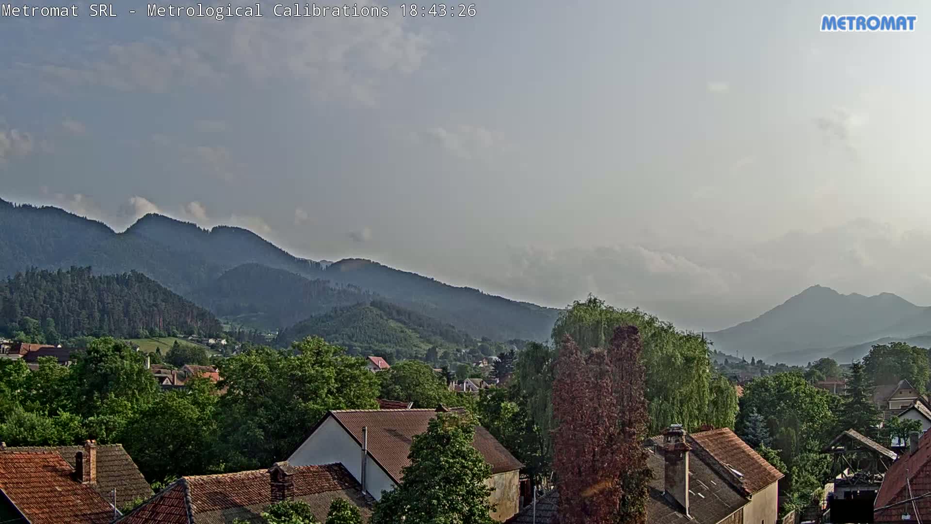 A partly cloudy sky overlooks a town nestled amongst green hills and mountains.