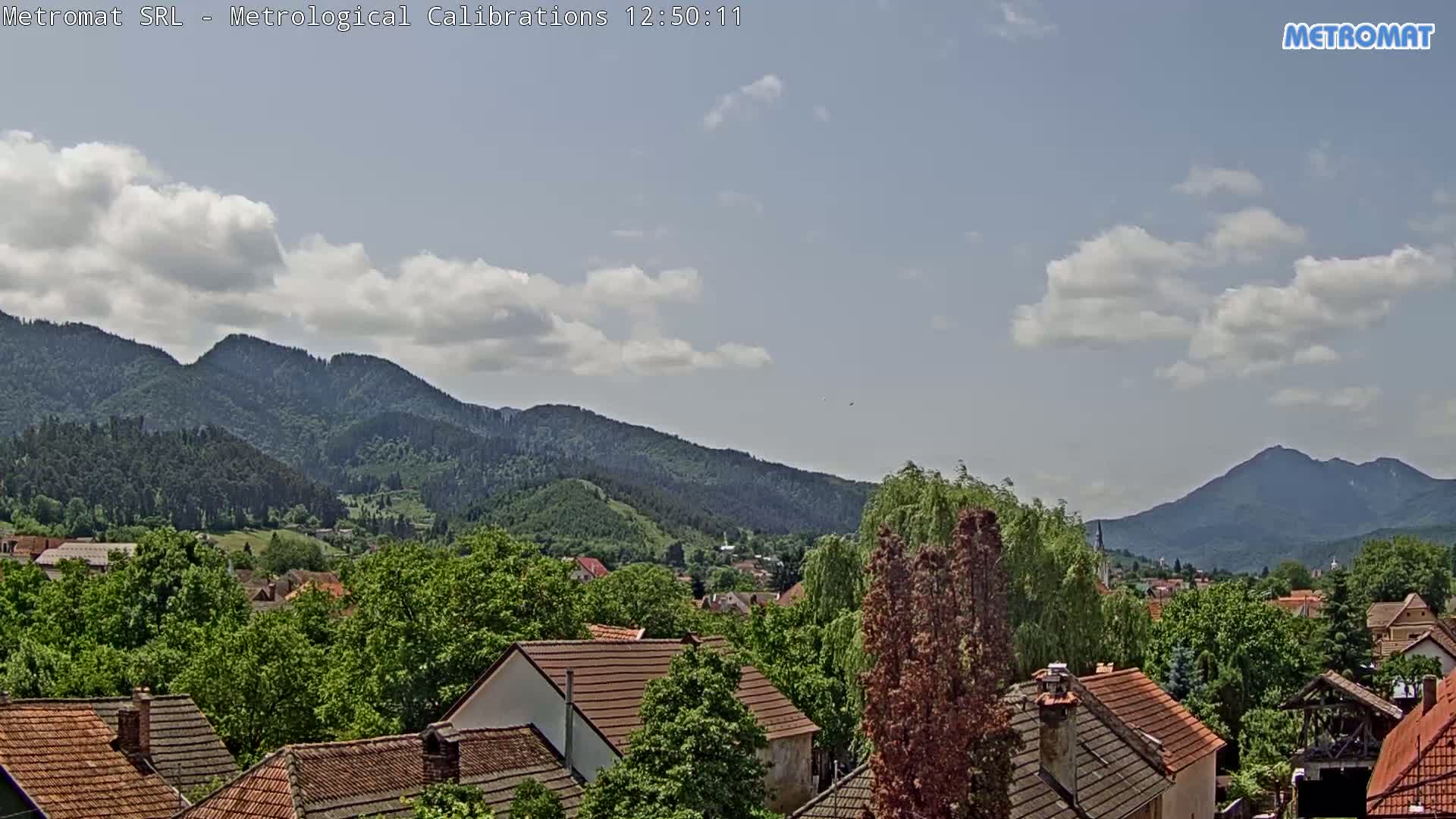 A partly cloudy sky overlooks a village nestled among green, forested mountains.