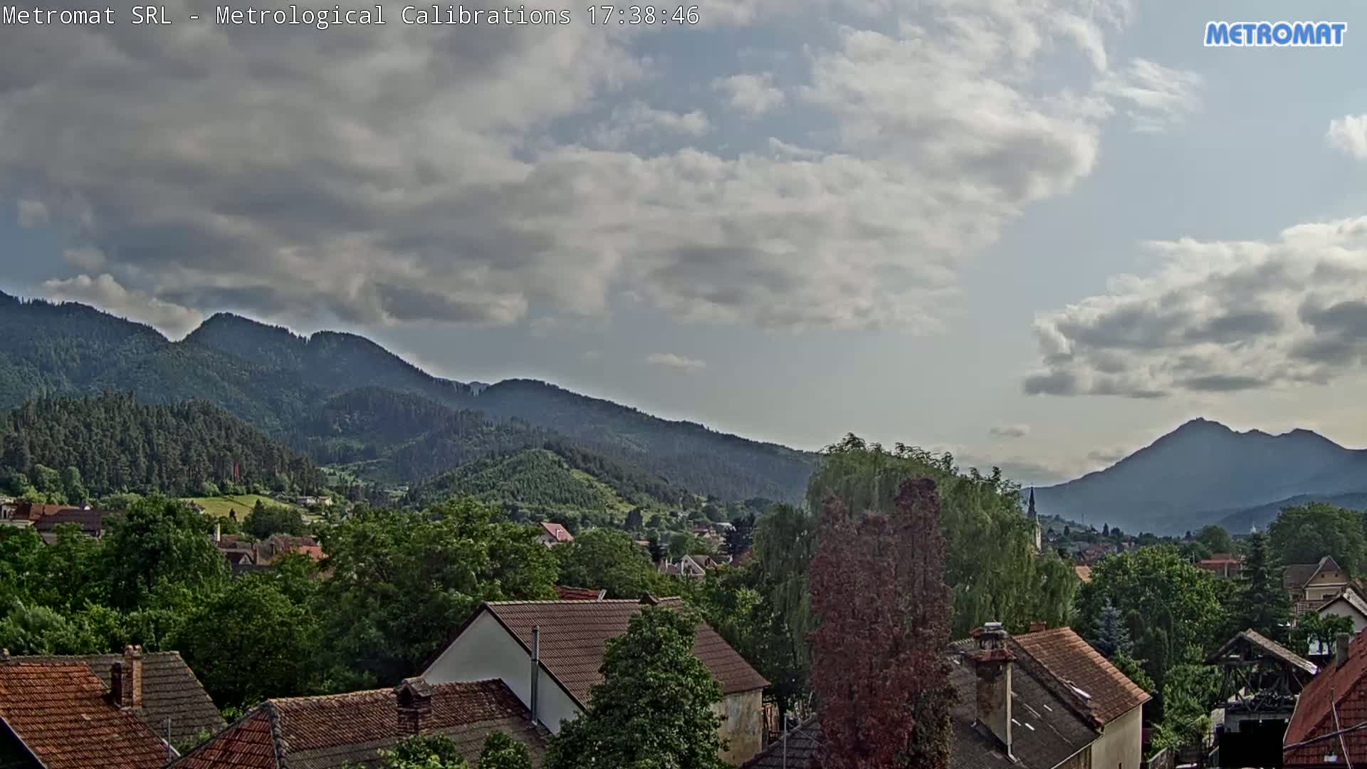 A partly cloudy sky overlooks a village nestled among green, forested mountains.