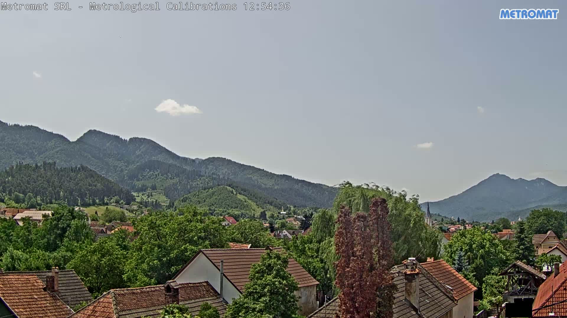 A mostly clear sky overlooks a town nestled among green, tree-covered mountains.