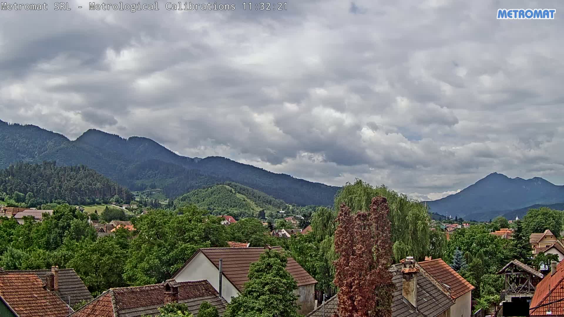 A partly cloudy sky overlooks a village nestled among green, tree-covered mountains.