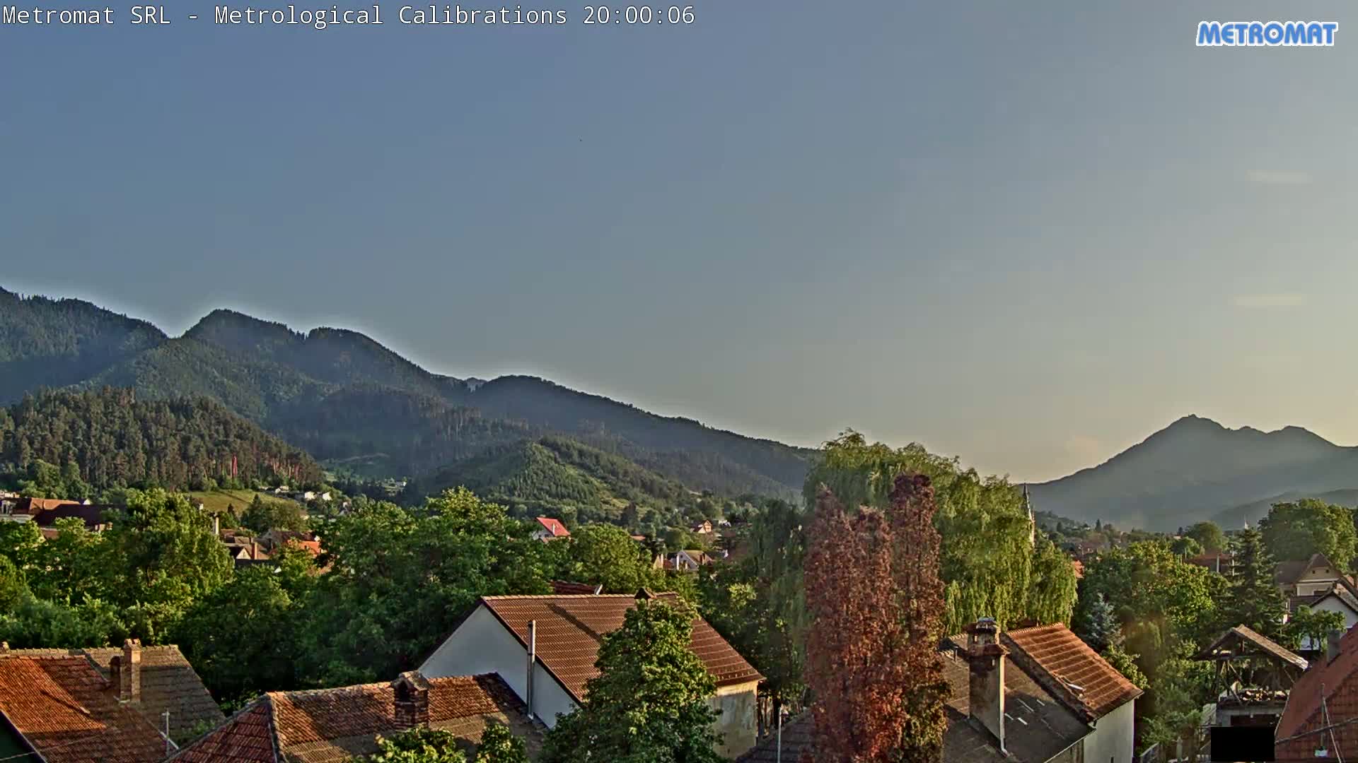 A clear evening view shows a small town nestled amongst lush green hills and mountains.