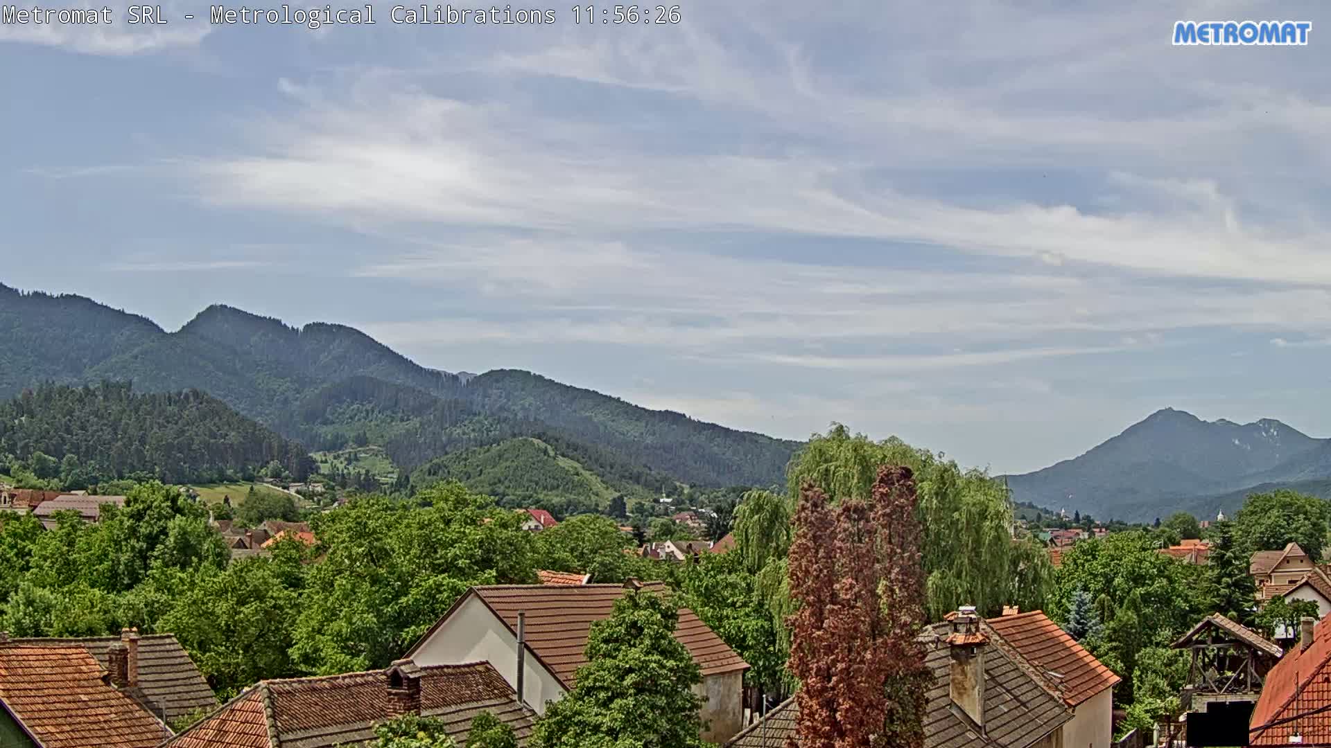 A partly cloudy sky overlooks a town nestled among green, tree-covered hills and mountains.