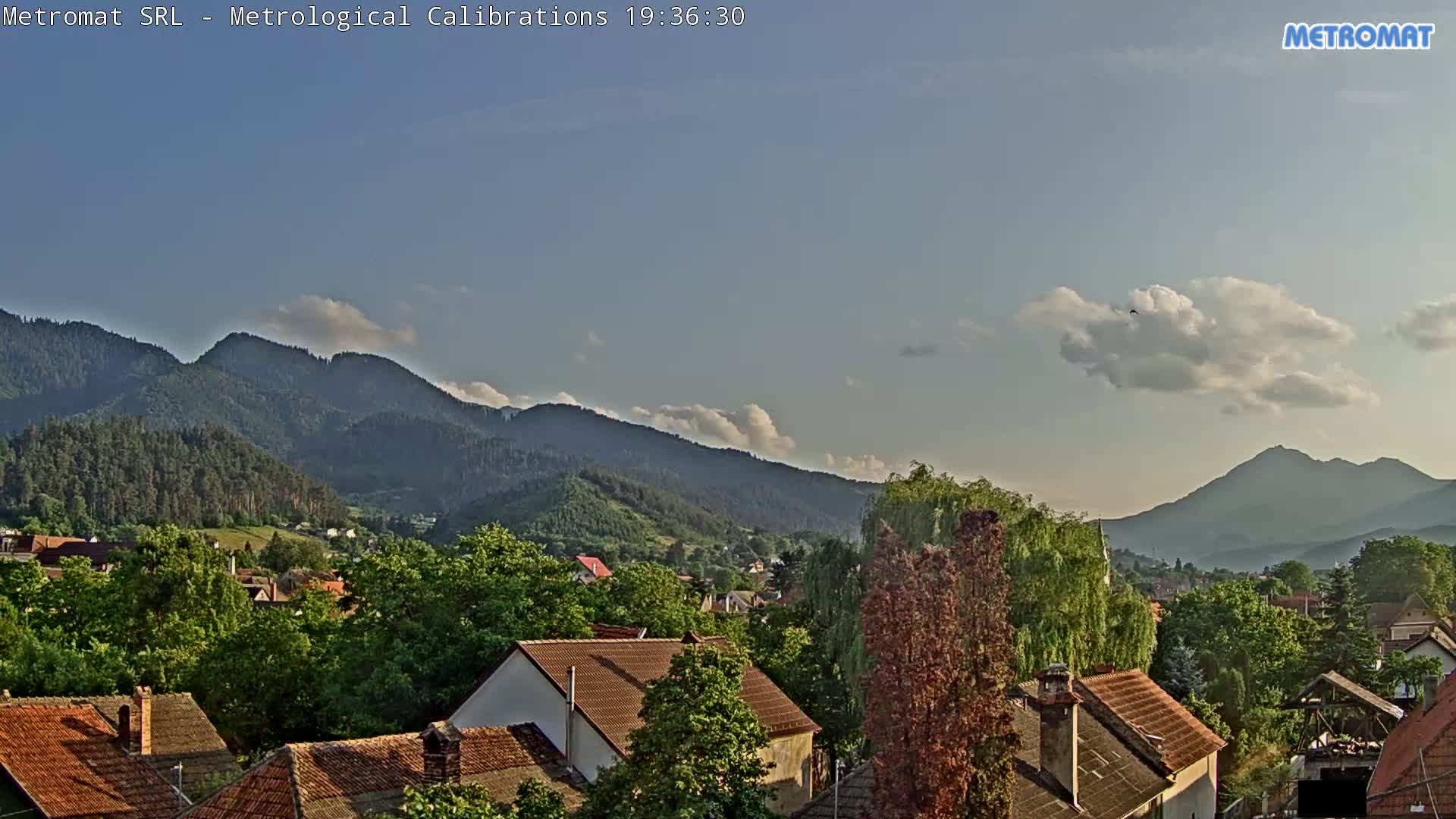 A partly cloudy sky overlooks a town nestled among green, forested mountains.