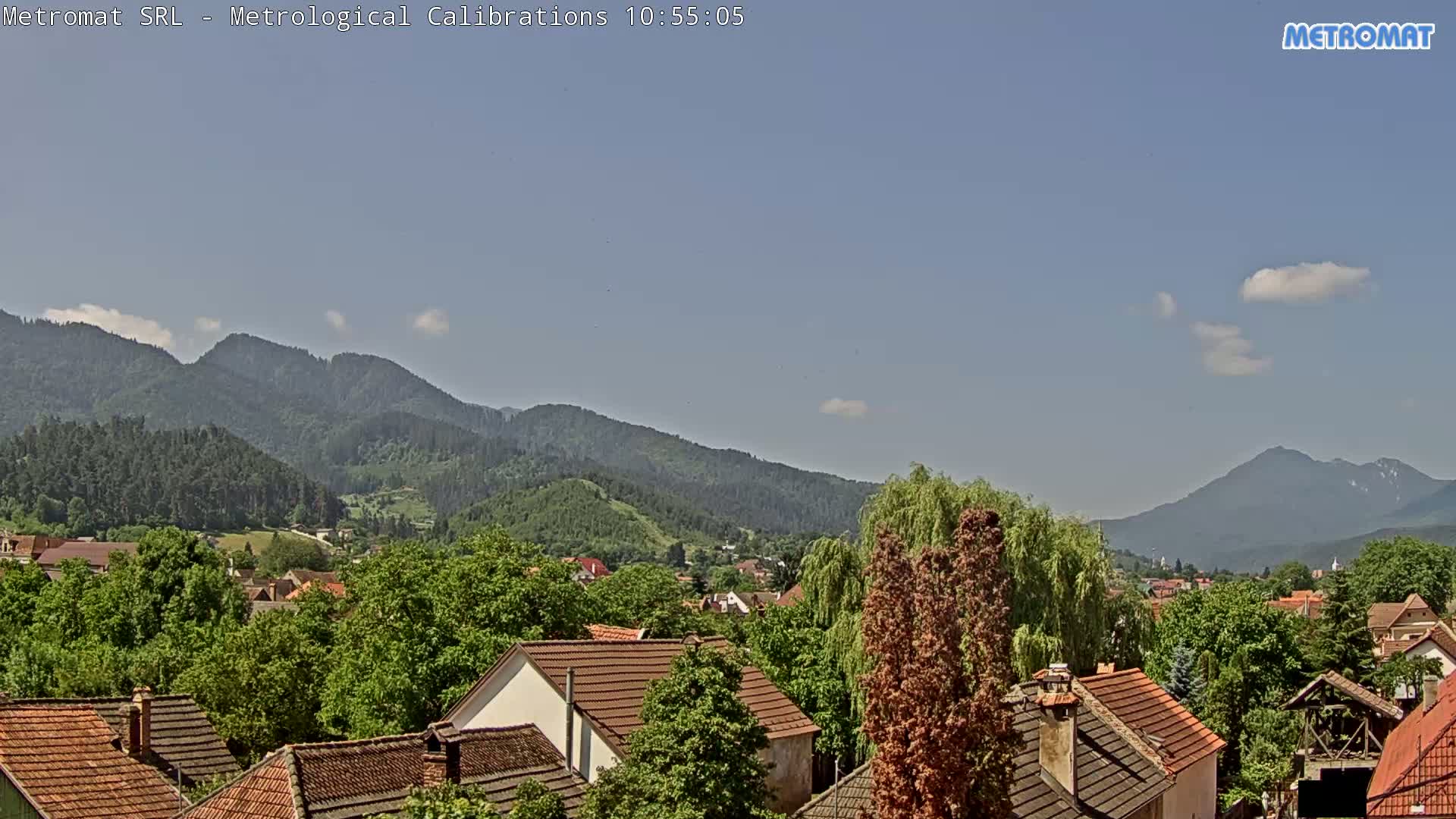 A partly sunny day reveals a small town nestled amongst lush green trees and mountains in the background.