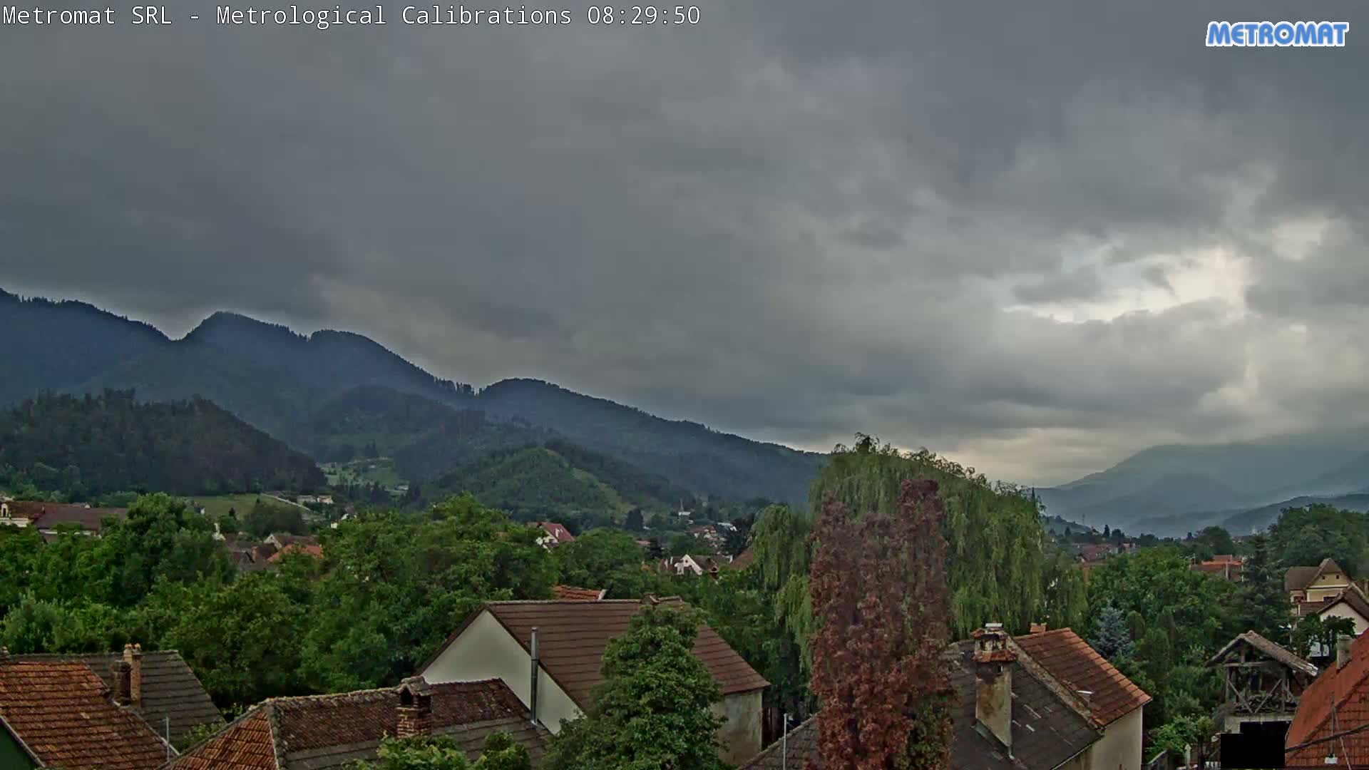 A view of a town nestled among green hills and mountains under a cloudy, overcast sky.