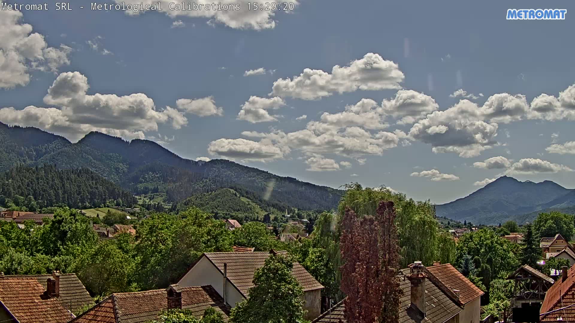 A partly cloudy sky overlooks a town nestled among green, forested mountains.