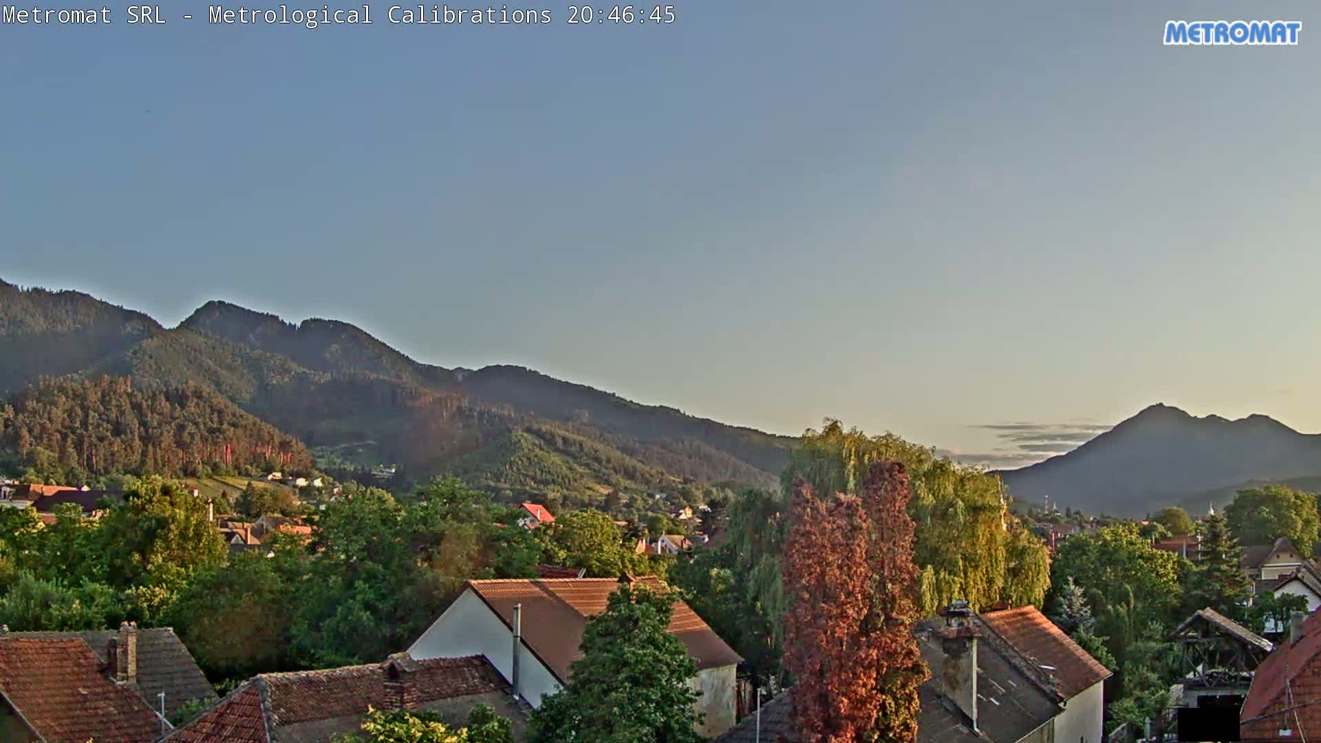 A clear evening sky overlooks a town nestled among green hills and mountains.