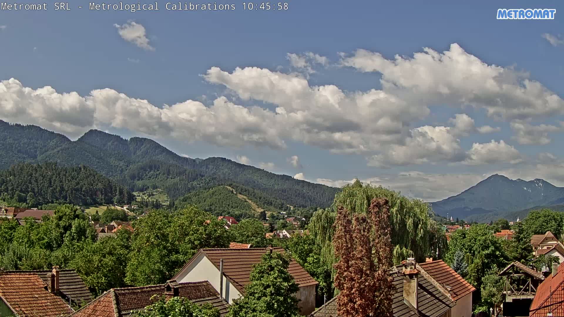 A partly cloudy sky overlooks a town nestled among green, tree-covered mountains.