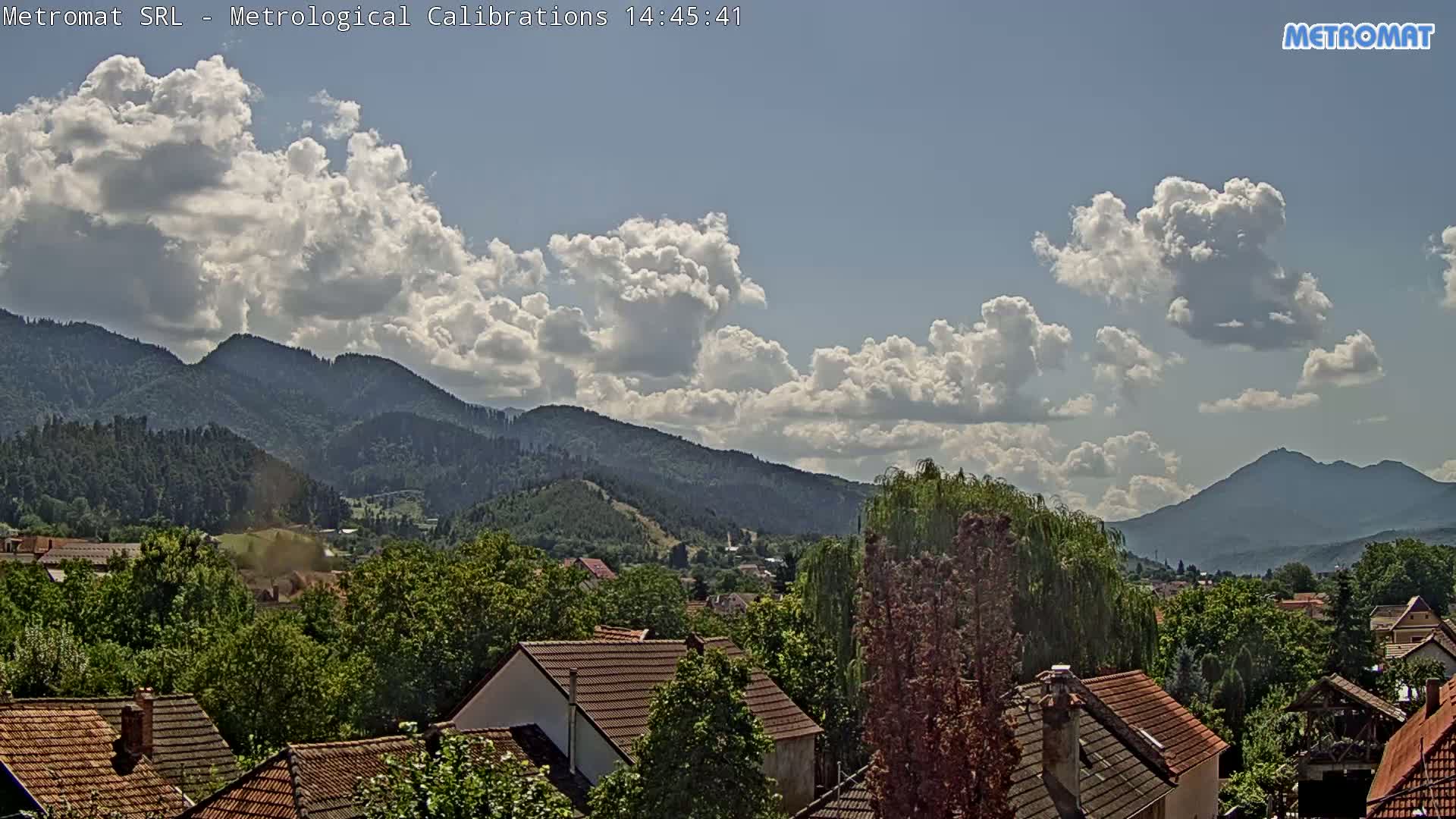 A clear, sunny day reveals a small town nestled among green trees and mountains.