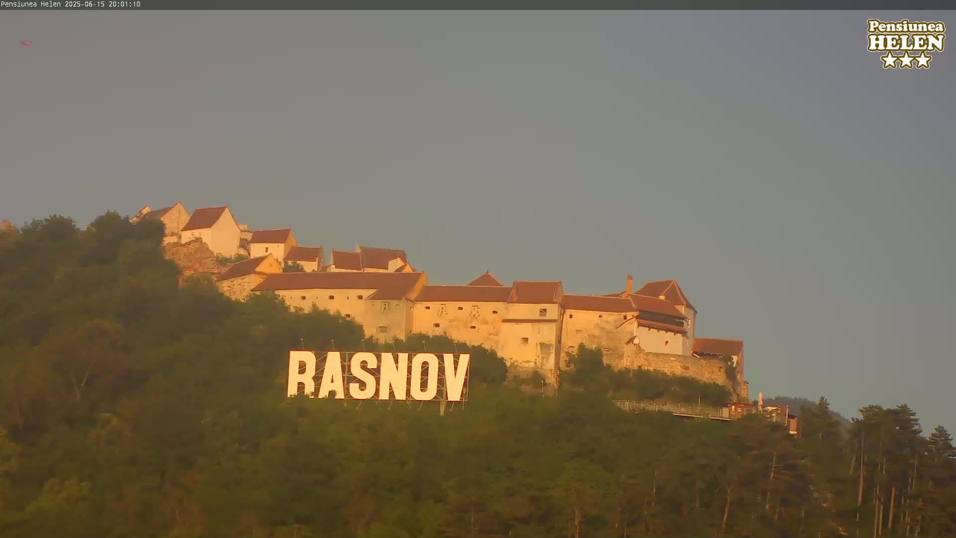 A large sign reading "RASNOV" sits below a hilltop castle under a pale, overcast sky.