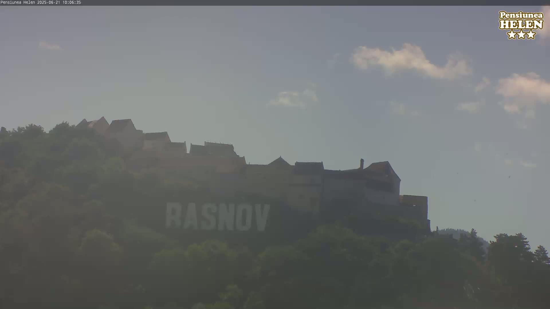 A castle sits atop a hill on a hazy day with a few clouds in the sky.
