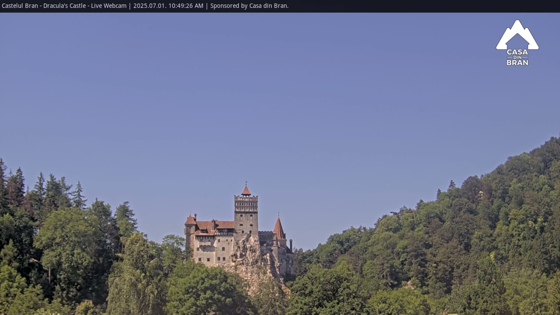 A medieval castle sits atop a rocky cliff, surrounded by lush green forests under a clear blue sky.
