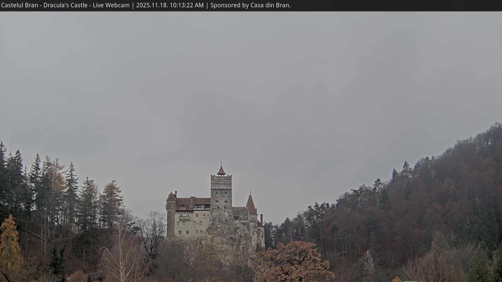 A medieval castle sits atop a rocky outcrop surrounded by lush green forests under a clear blue sky.