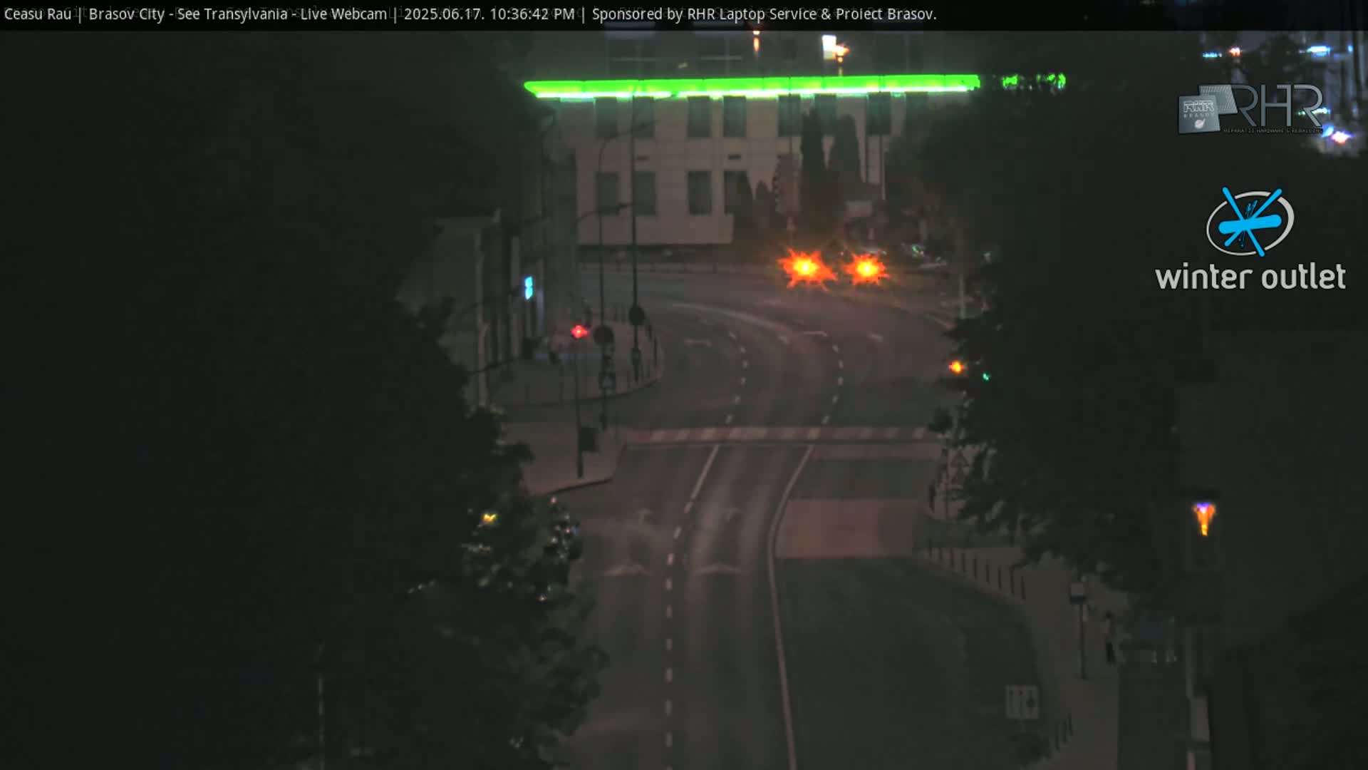 A nighttime view of a road intersection with a building illuminated by a green light, featuring minimal traffic under dark, clear conditions.