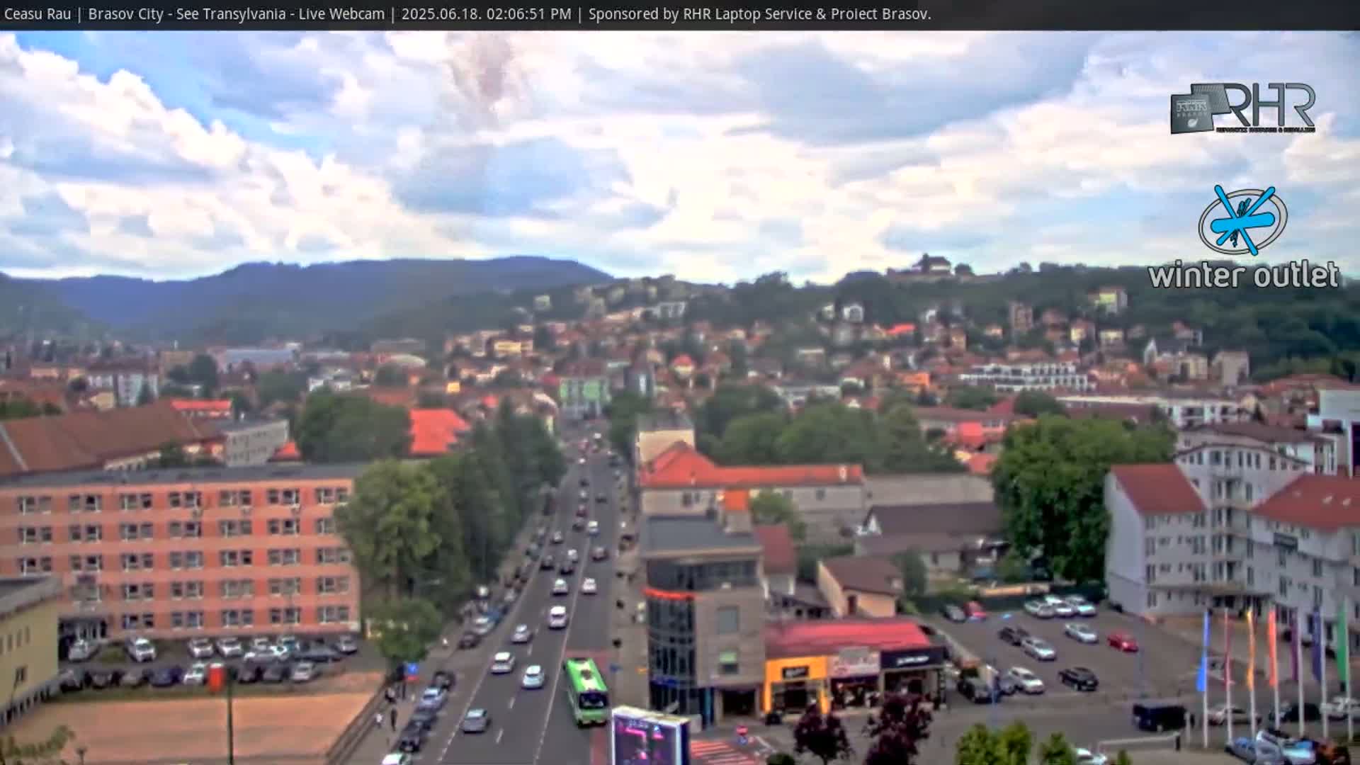 A partly cloudy day overlooks a city with a main road, buildings, and parked cars.