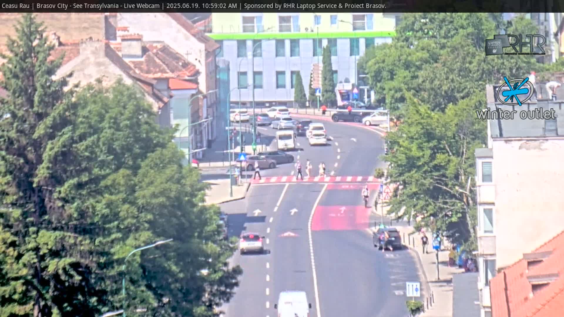 A sunny day overlooking a city street with cars and pedestrians, green trees lining the sides of the road.