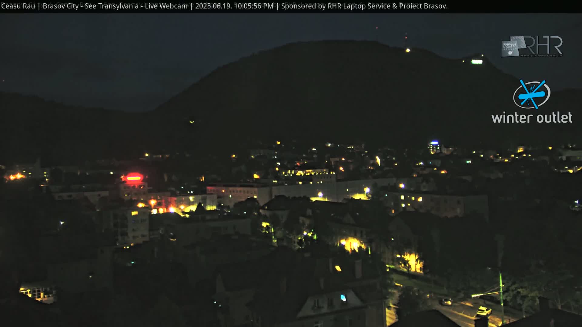 A nighttime view of a city nestled beneath a dark hill, illuminated by scattered streetlights.