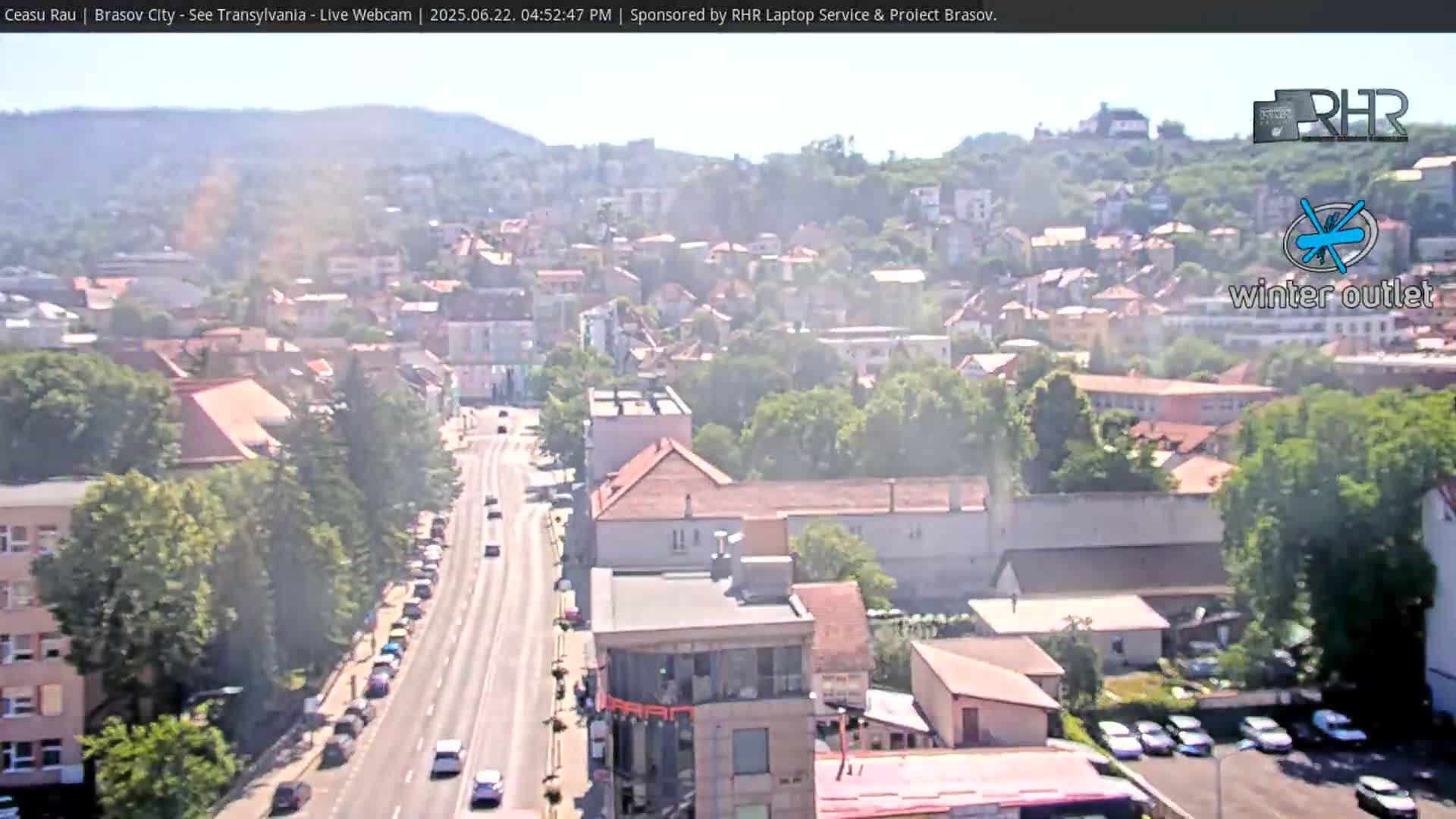 A hazy, sunny day reveals a long road cutting through a city nestled between hills, with numerous buildings and parked cars visible.