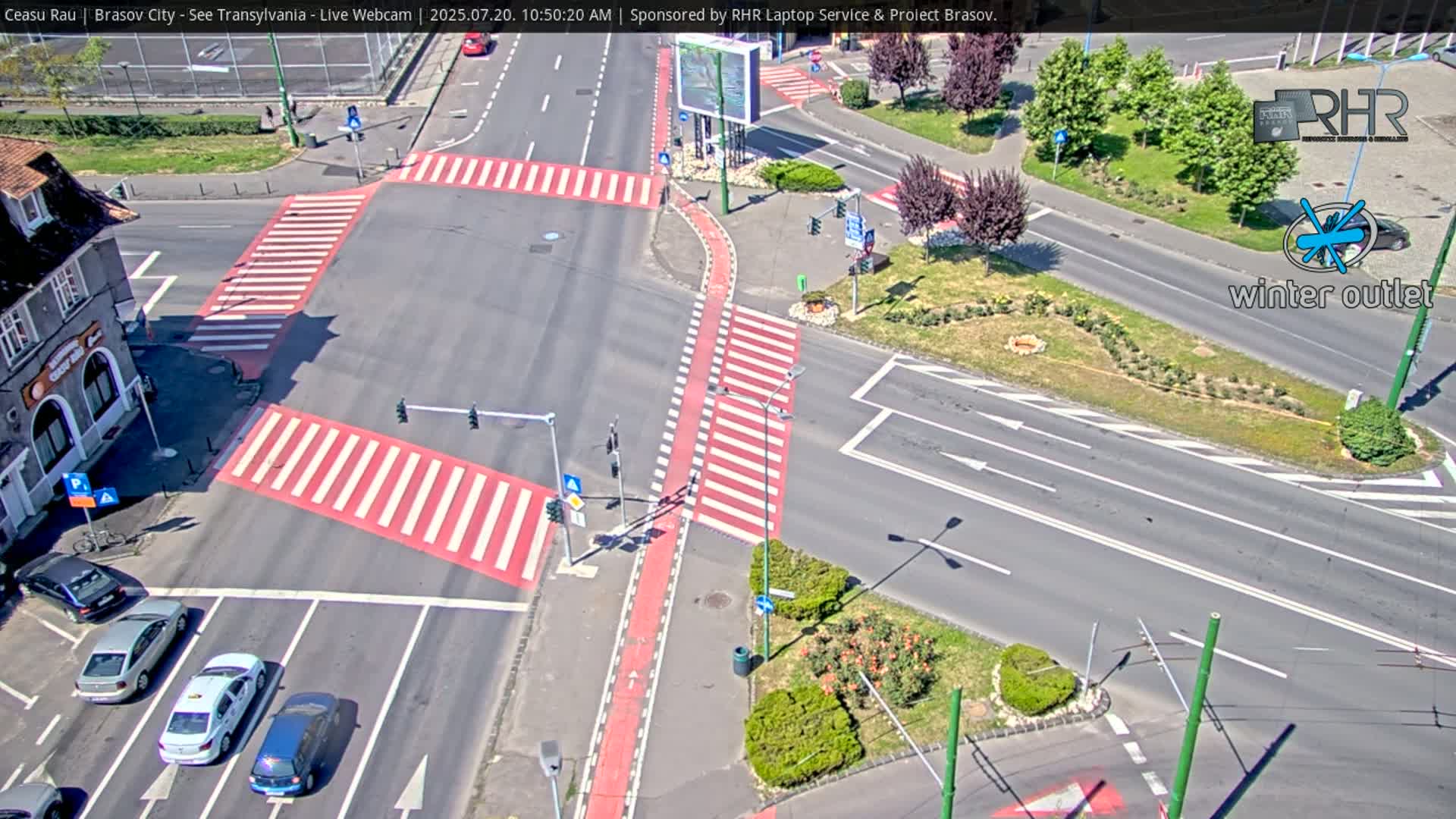 An aerial view of a roadway intersection with several cars and pedestrians, under sunny conditions.