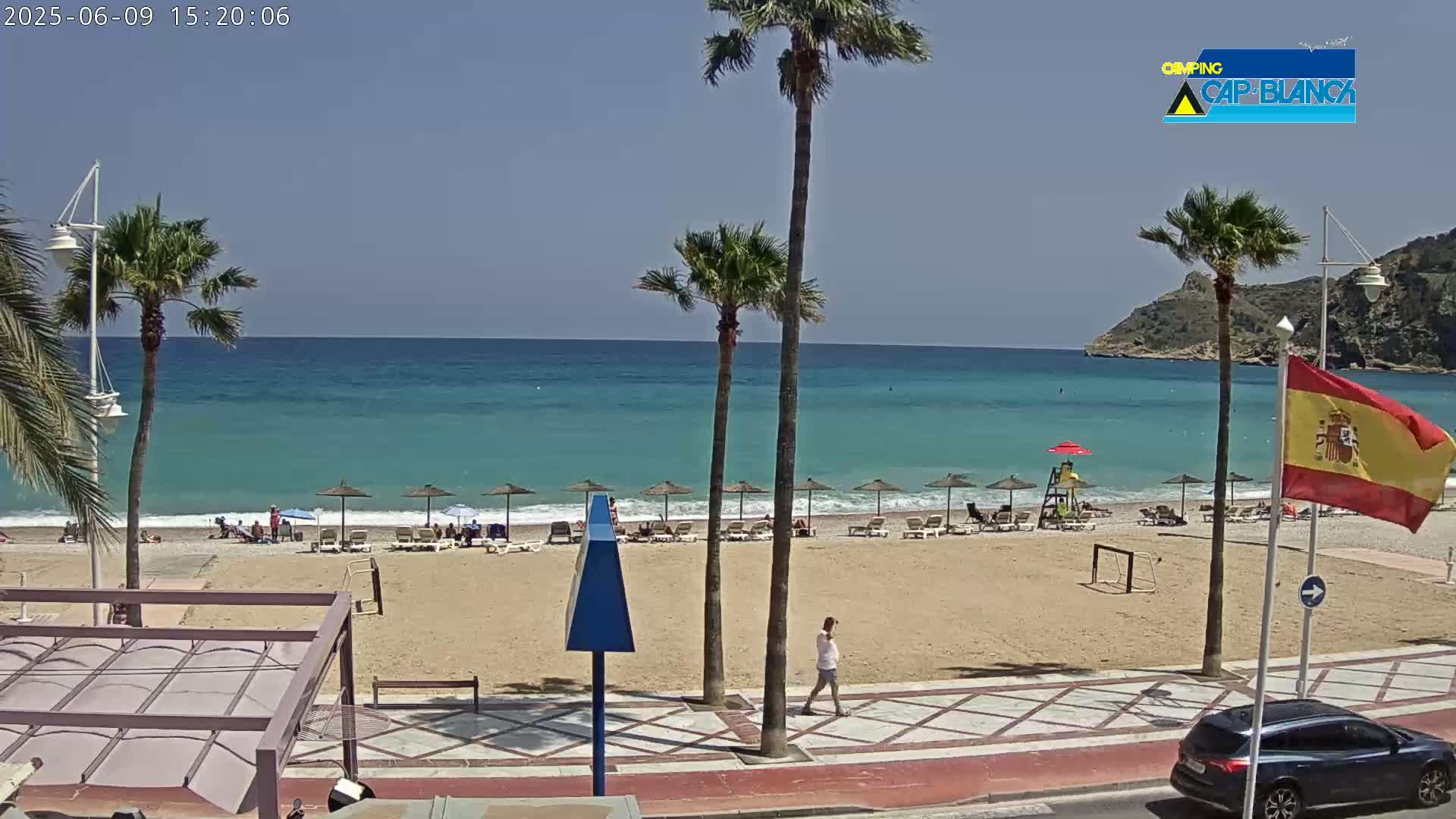 A sandy beach with turquoise water, palm trees, and a few people, under sunny skies.