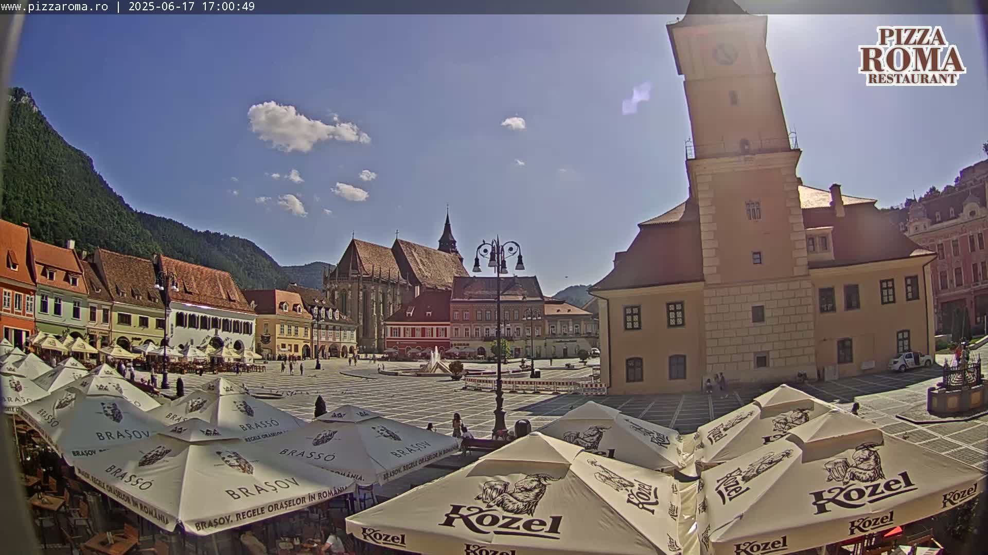 A sunny European town square with several buildings, a church, and numerous outdoor cafe umbrellas.