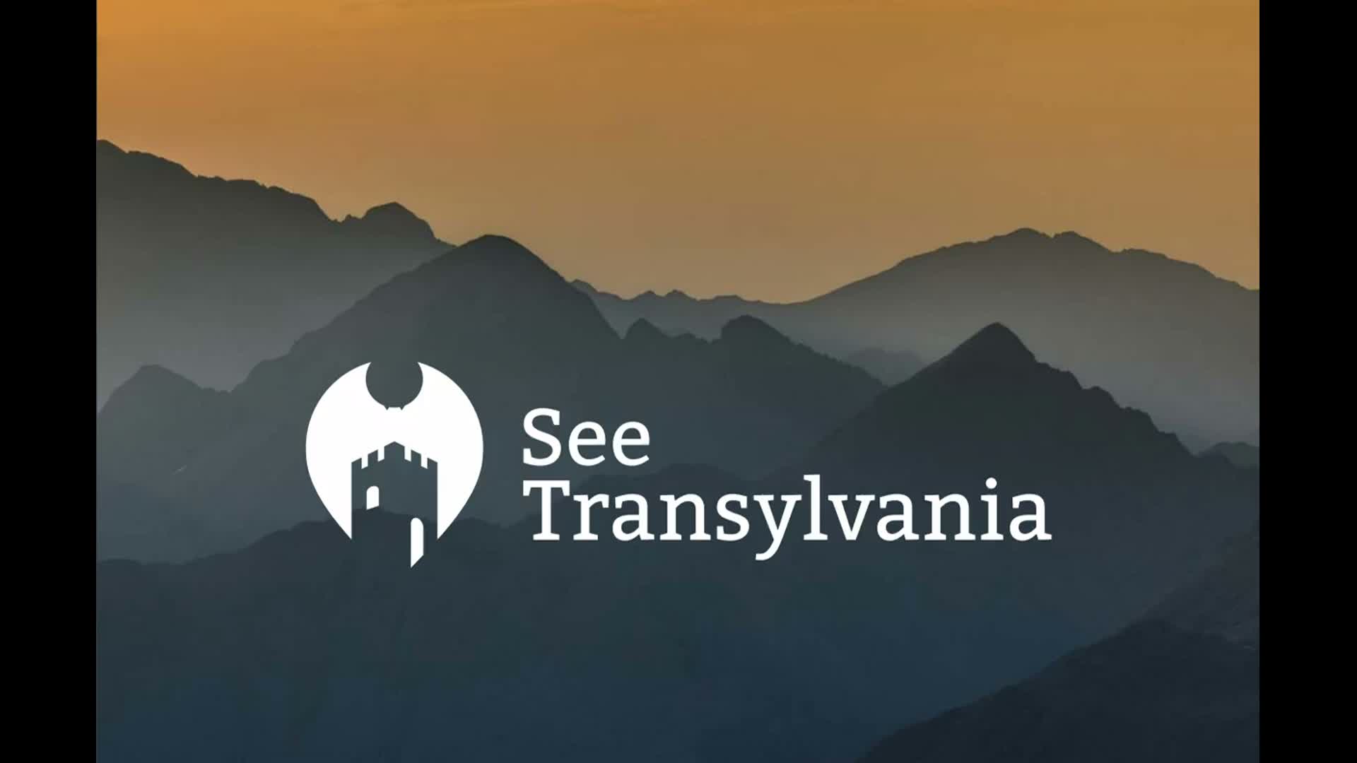 A layered mountain range is silhouetted against a hazy twilight sky that transitions from warm orange at the top to lighter blue-gray near the peaks.