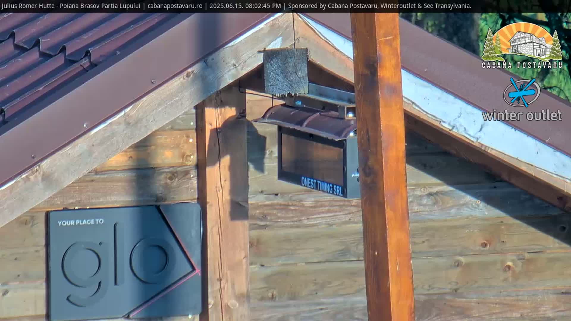 A wooden structure with a brown roof is partially visible in sunny conditions, with various electronic devices attached.