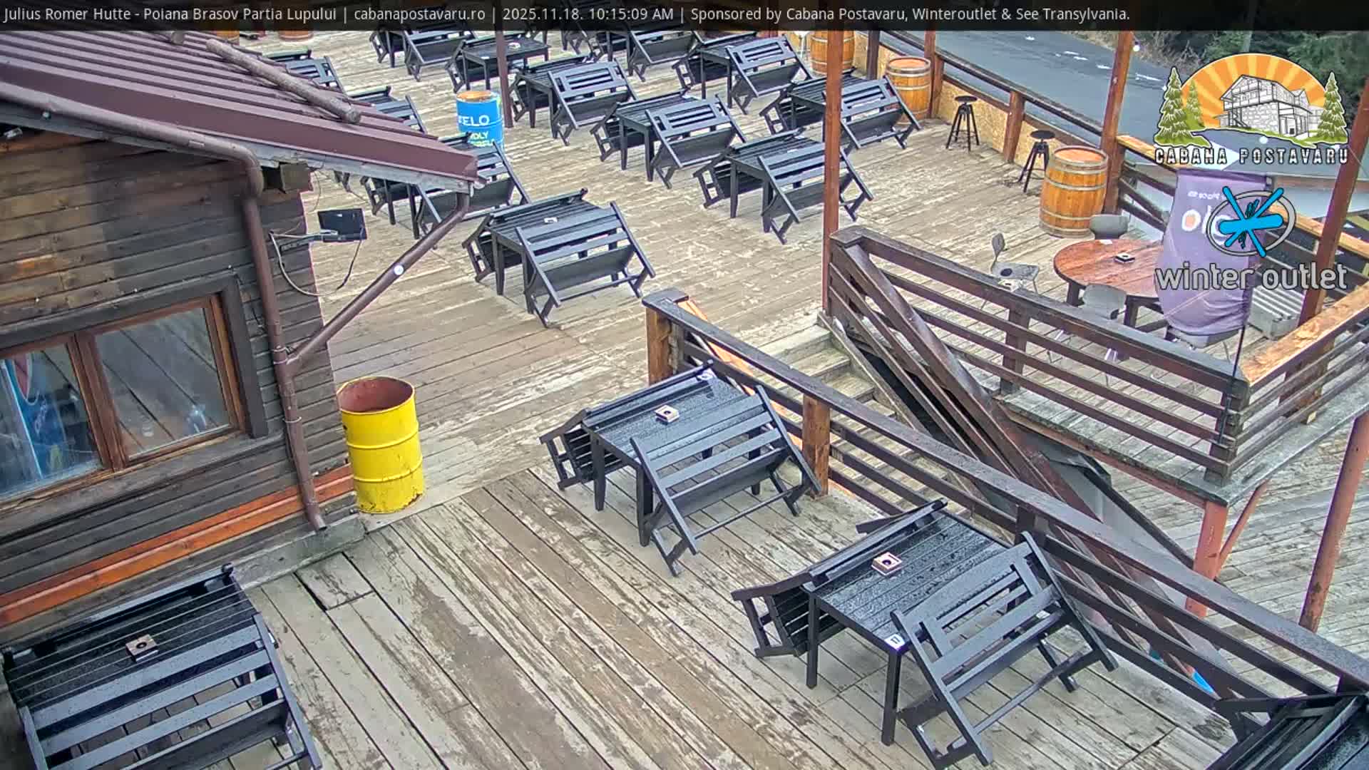 An expansive, multi-level wooden outdoor deck, likely part of a rustic building visible on the left, is covered with numerous dark, mostly folded or tipped, picnic tables and benches, appearing wet and deserted under overcast conditions.
