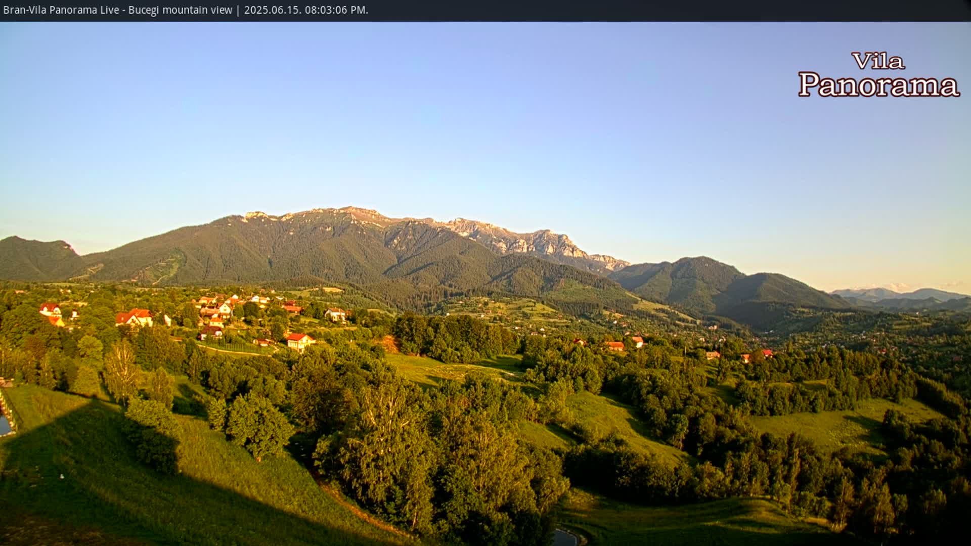 A village nestled in a valley, surrounded by lush green hills and mountains under a clear, bright sky.