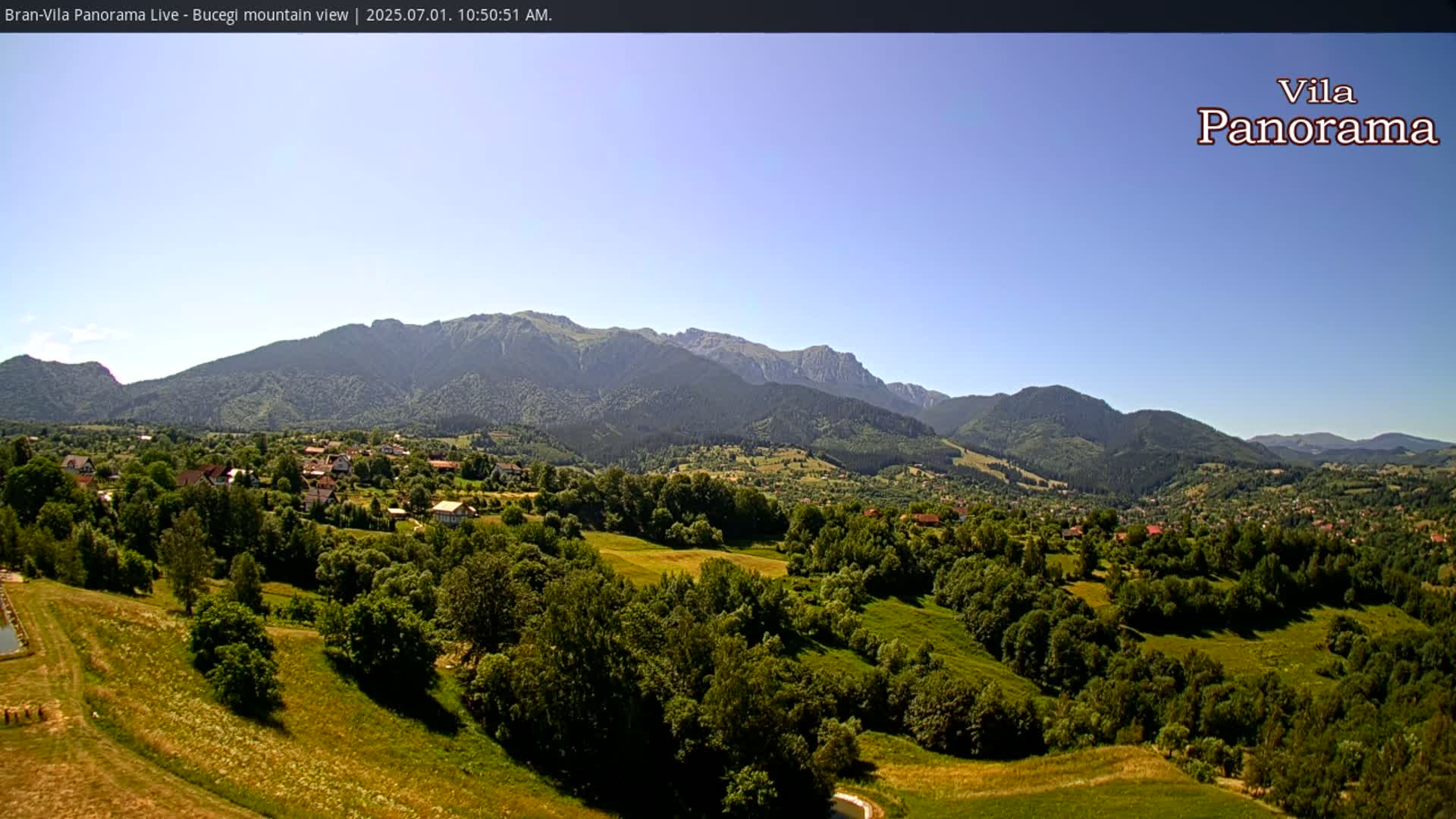 A sunny day reveals a verdant valley dotted with houses, nestled beneath a majestic mountain range.