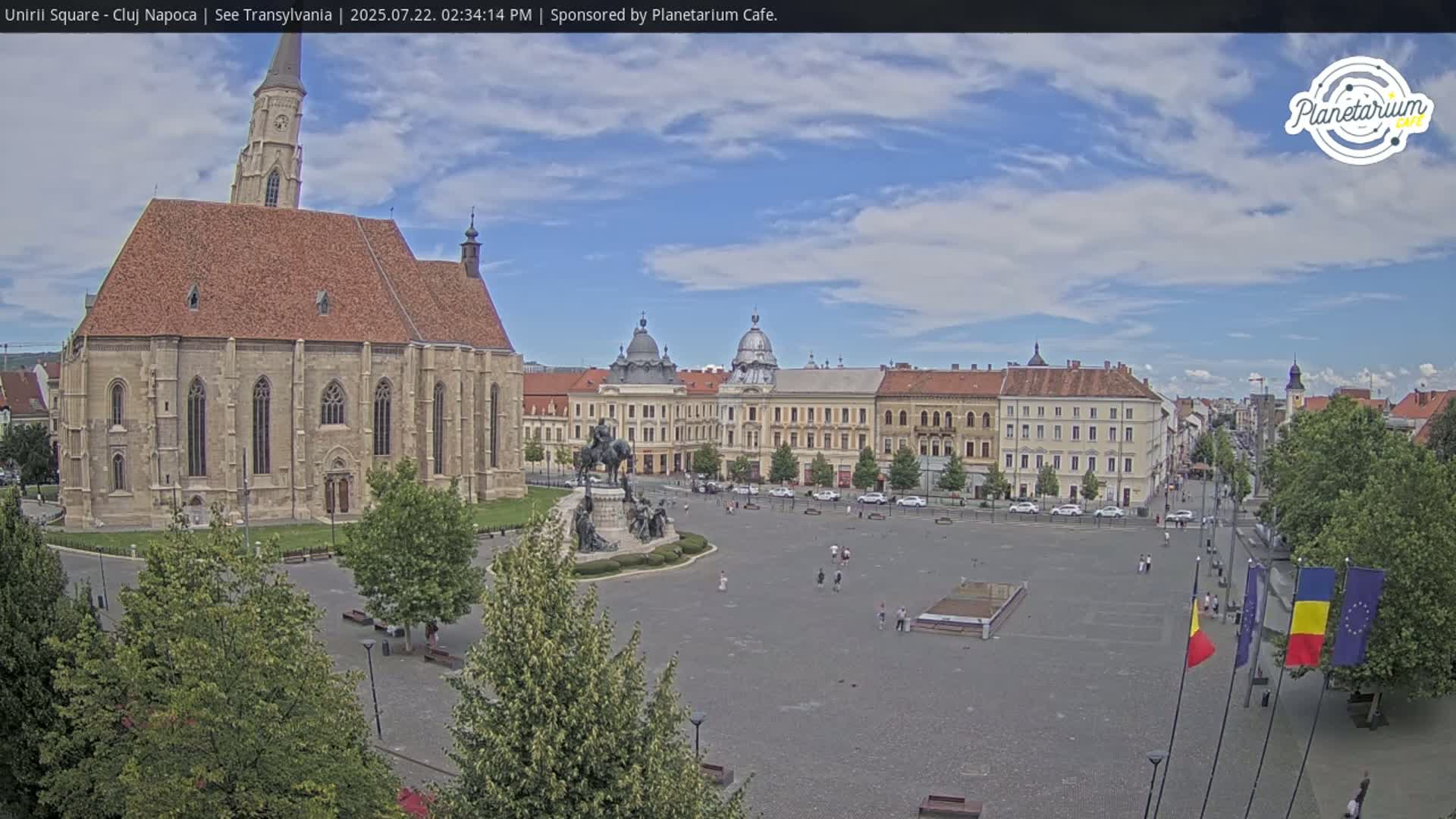 A large town square with a church and several buildings is seen on a partly cloudy day.