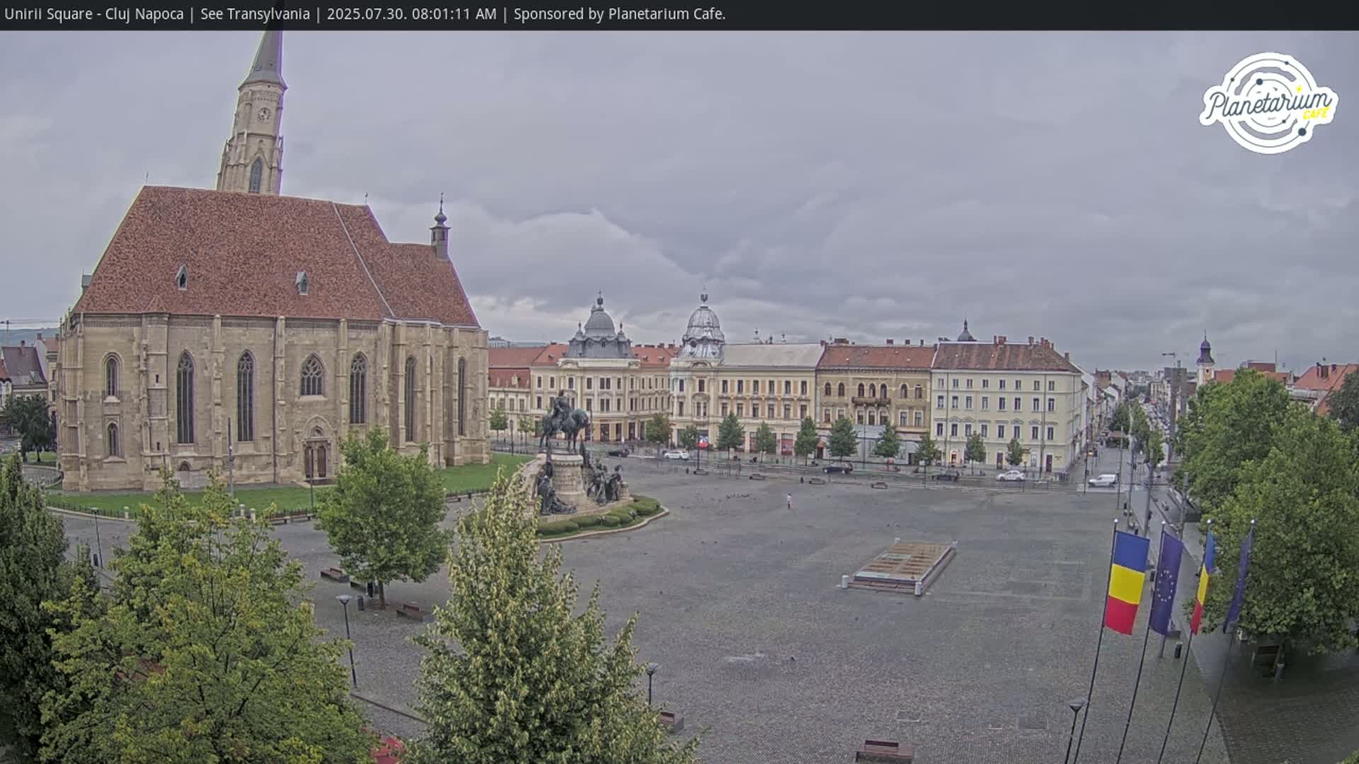 A large town square with a church and several buildings is seen on a partly cloudy day.
