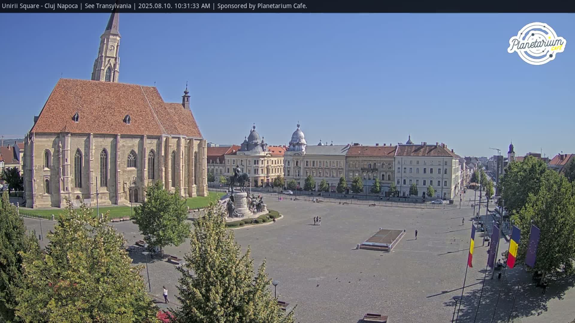 A large, open square with a church and several buildings is shown on a sunny day.