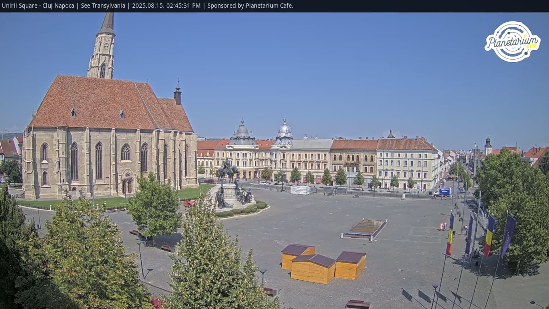 A large, open square with a church and several buildings is shown on a sunny day.