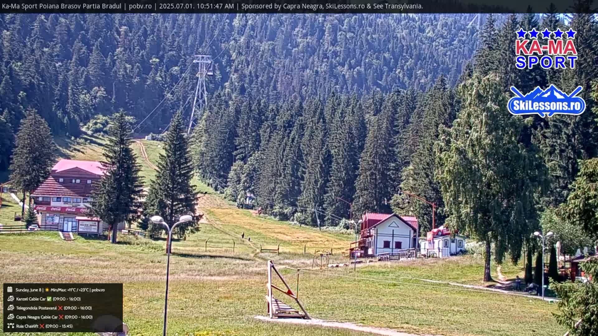 A sunny mountain landscape features a ski lift, several buildings, and a grassy area dotted with evergreen trees.