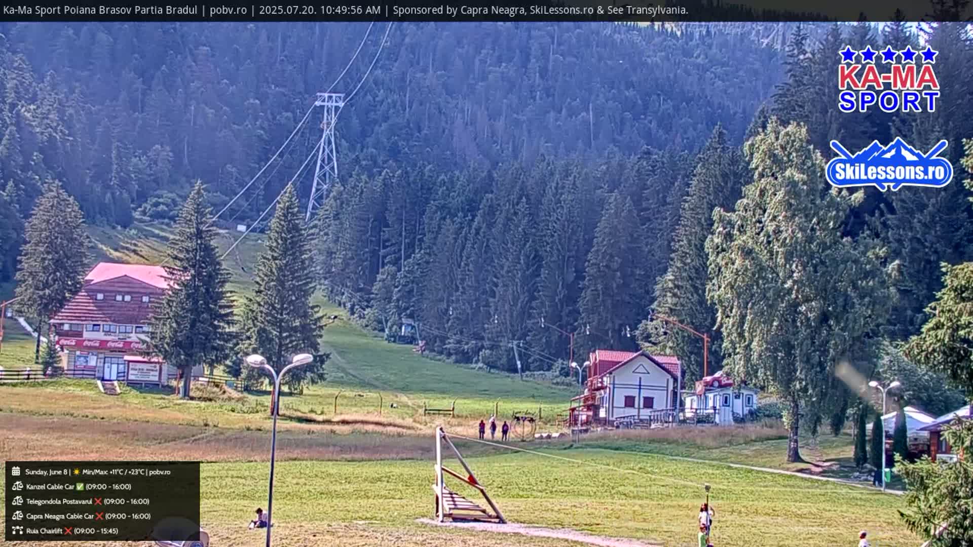 A sunny day at a ski resort shows a grassy area with a few people, a small building, and a chairlift ascending a forested hillside.