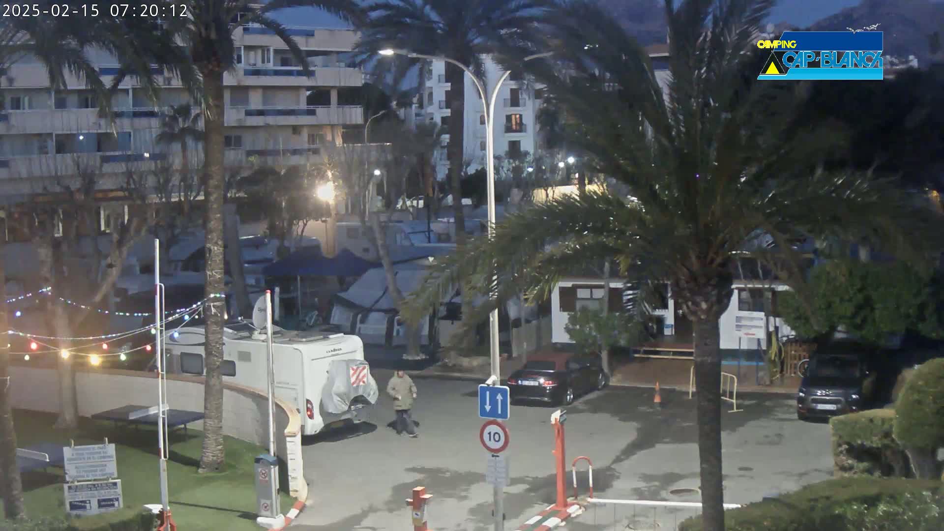 A nighttime scene shows a campground with RVs, cars, and palm trees, under a dark sky.