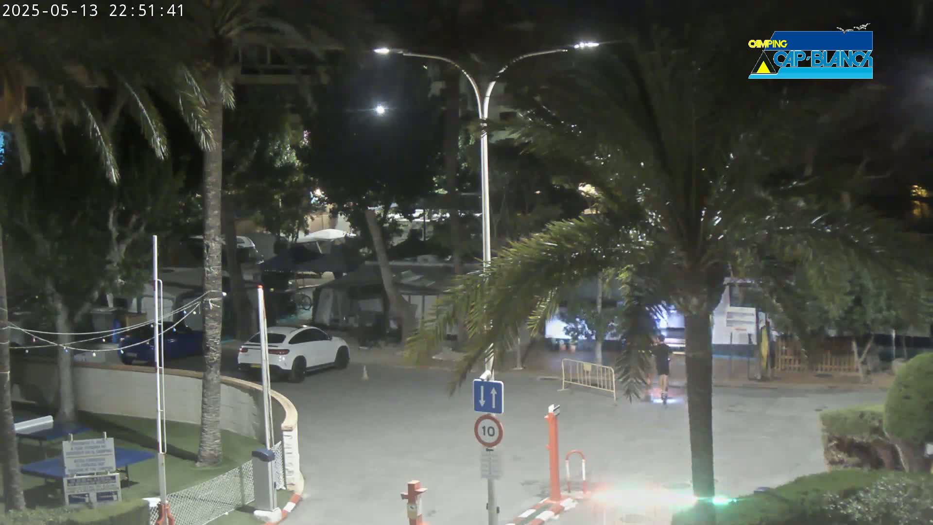 A nighttime view of a parking lot with palm trees, cars, and several campers or RVs, under a clear sky.