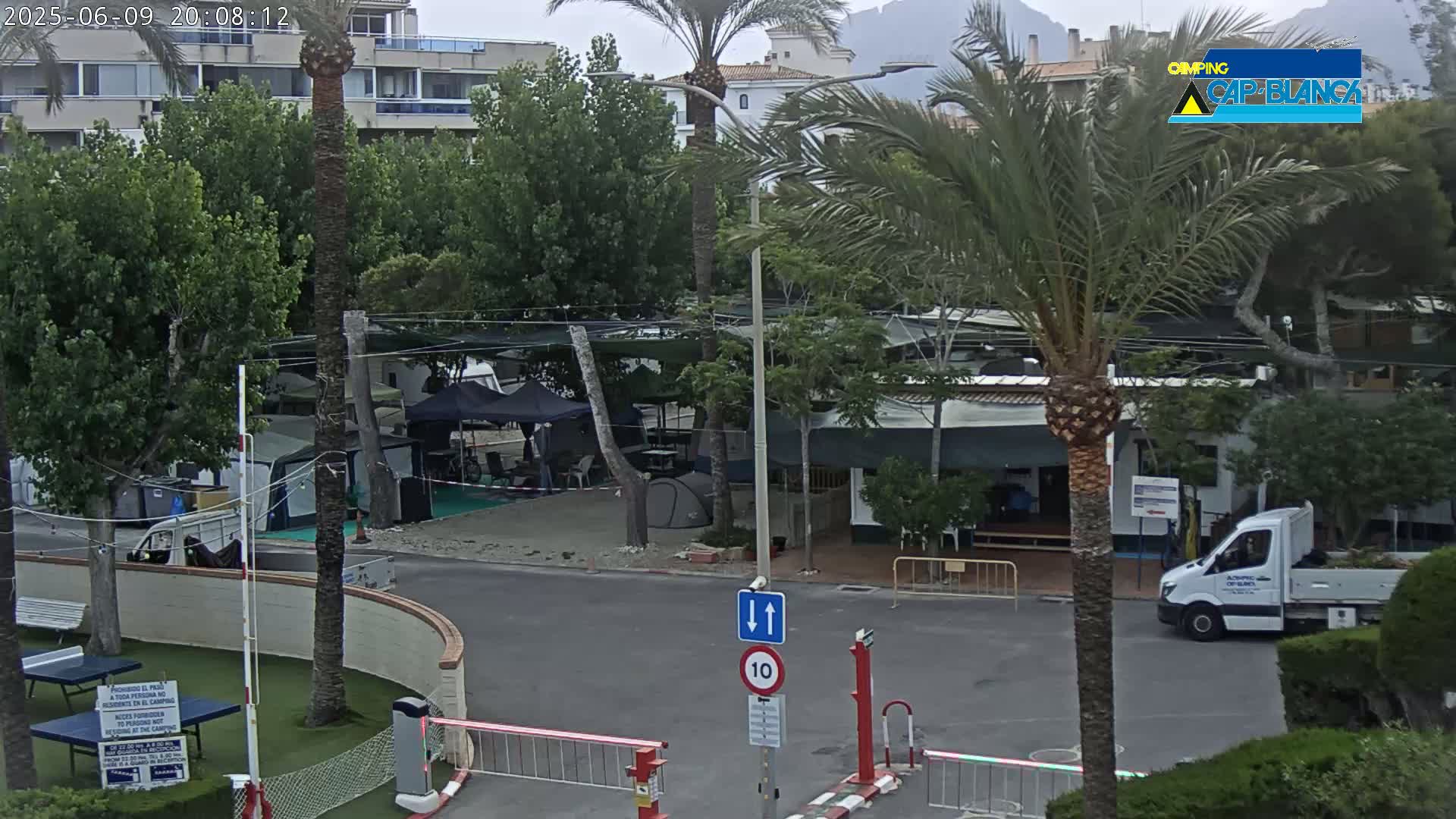 A campground with numerous tents and caravans is situated near a multi-story building under an overcast sky.