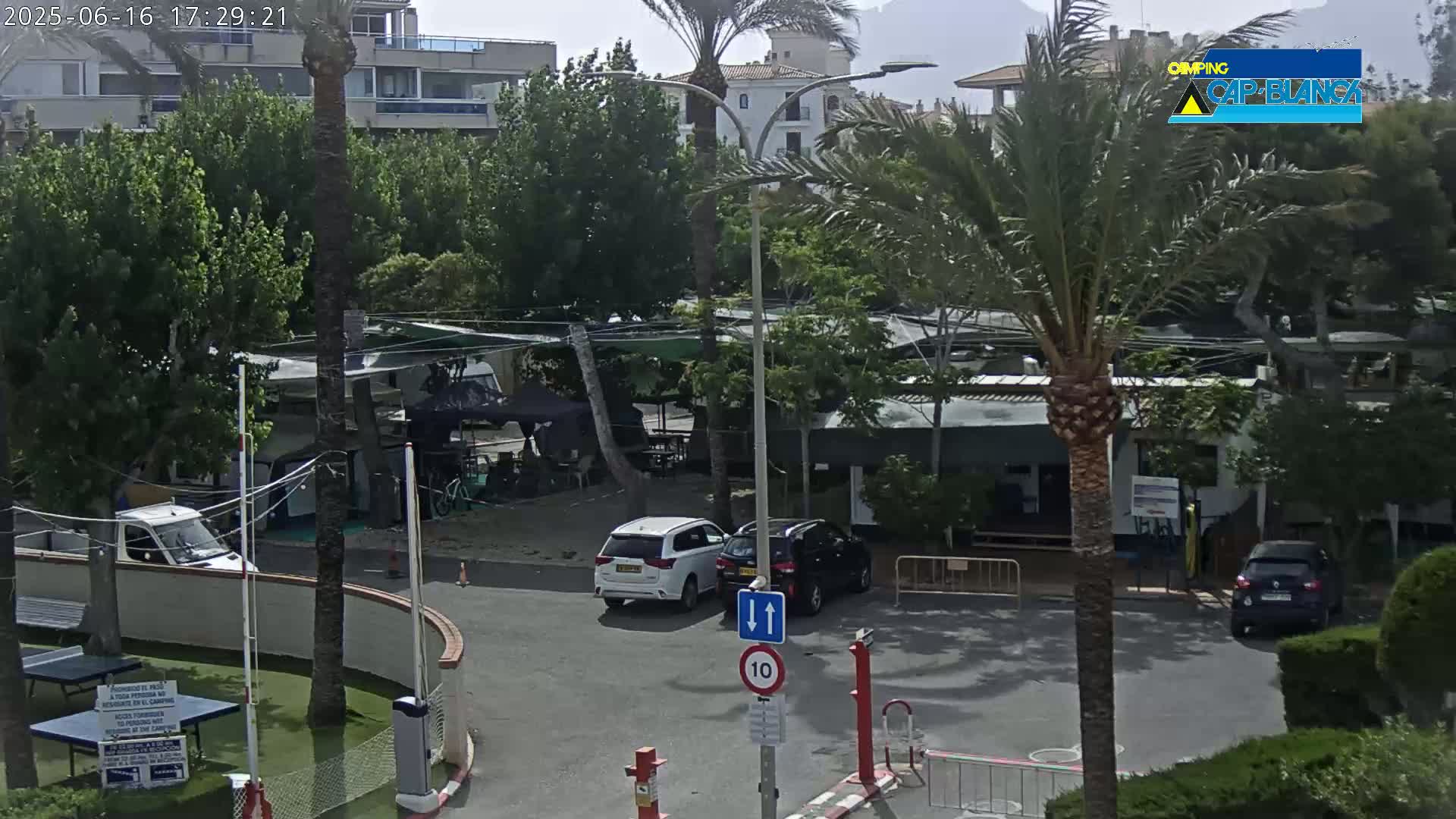 A slightly hazy, daytime view of a campground with several vehicles parked near buildings and palm trees.